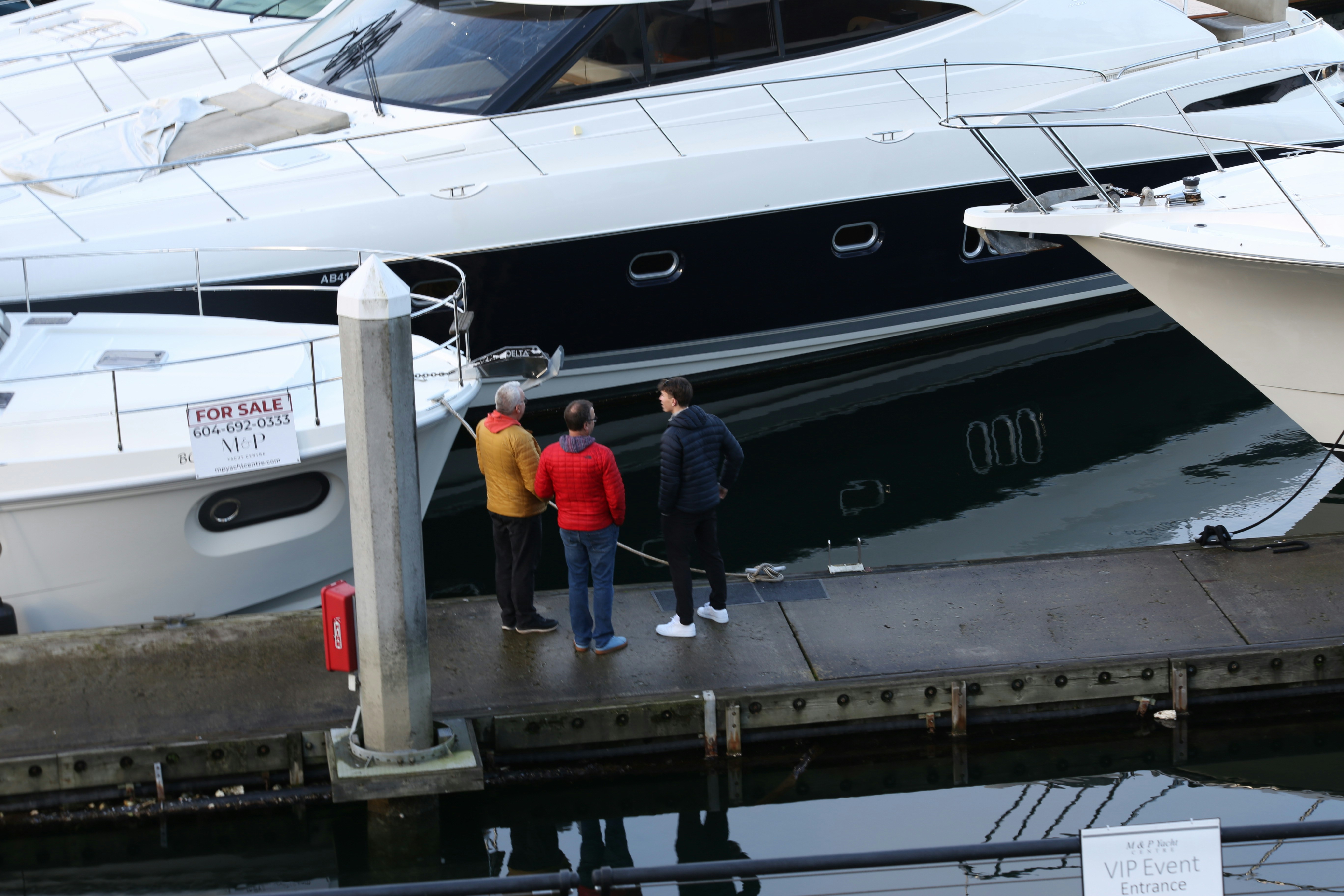 Three people stand on a dock next to yachts.