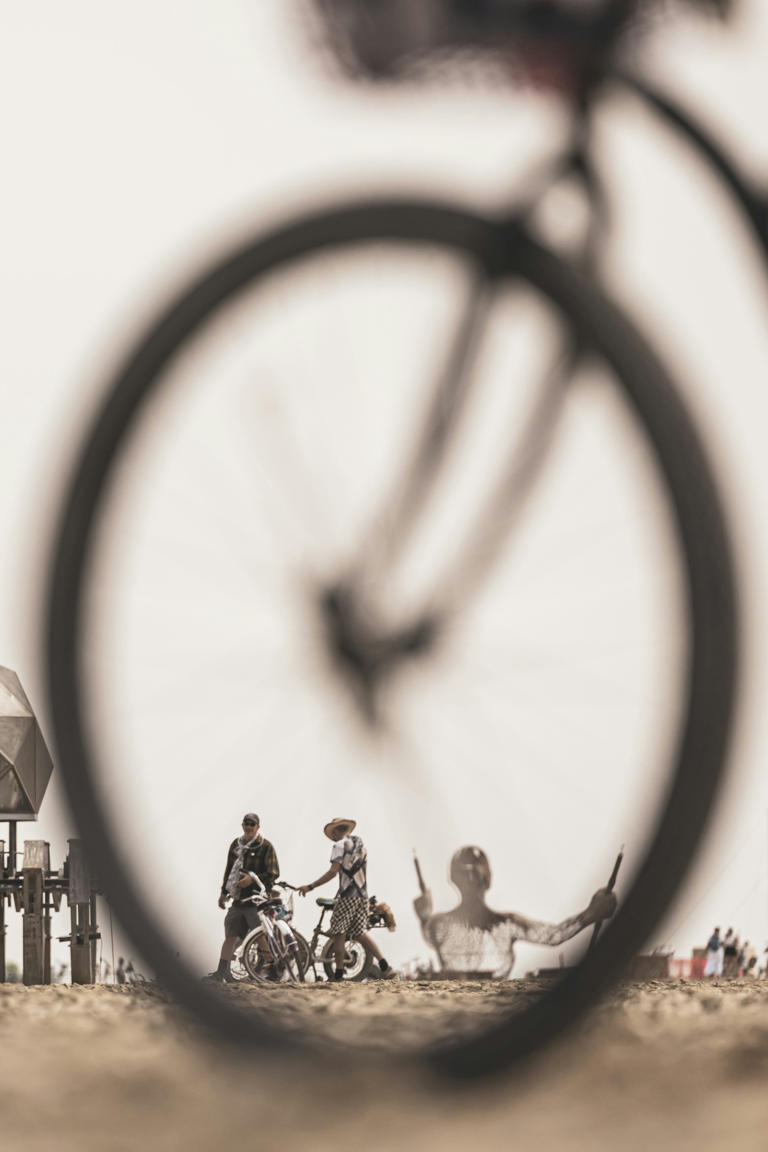 People and sculpture seen through bicycle wheel