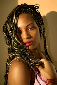 Woman with braided hair and bold makeup poses.