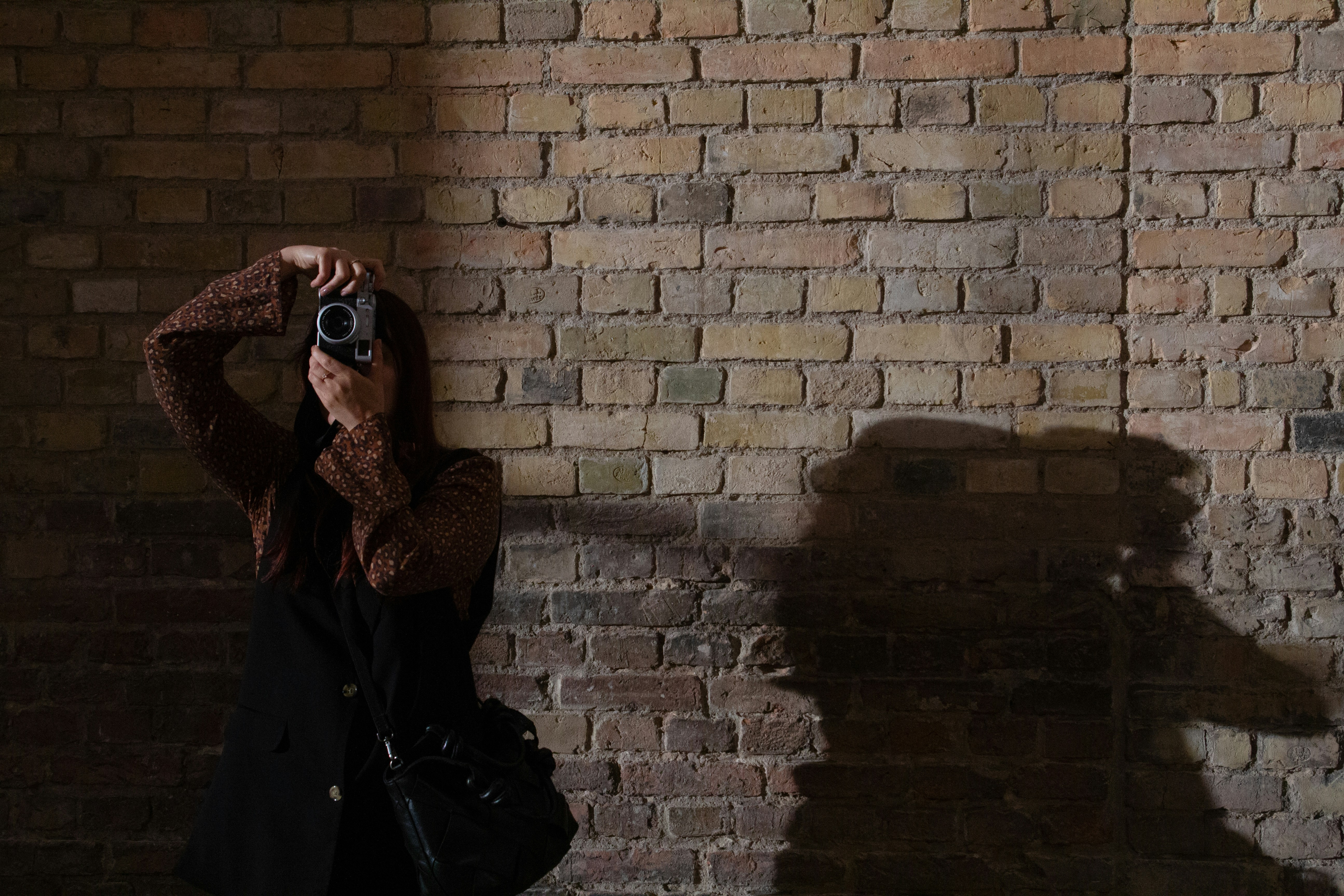 Woman taking a photo in front of a brick wall.