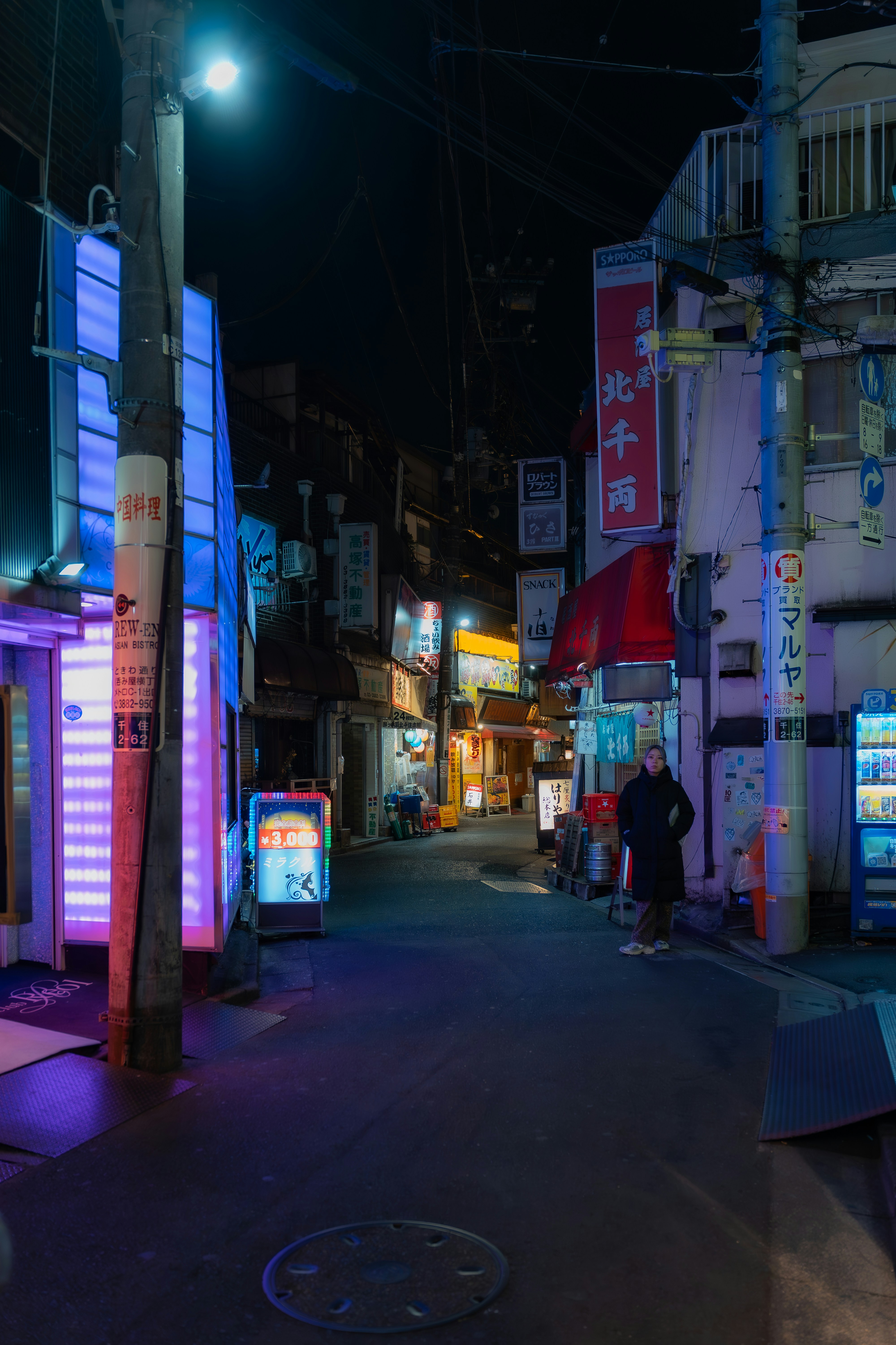 A solitary person stands on a neon-lit street at night.