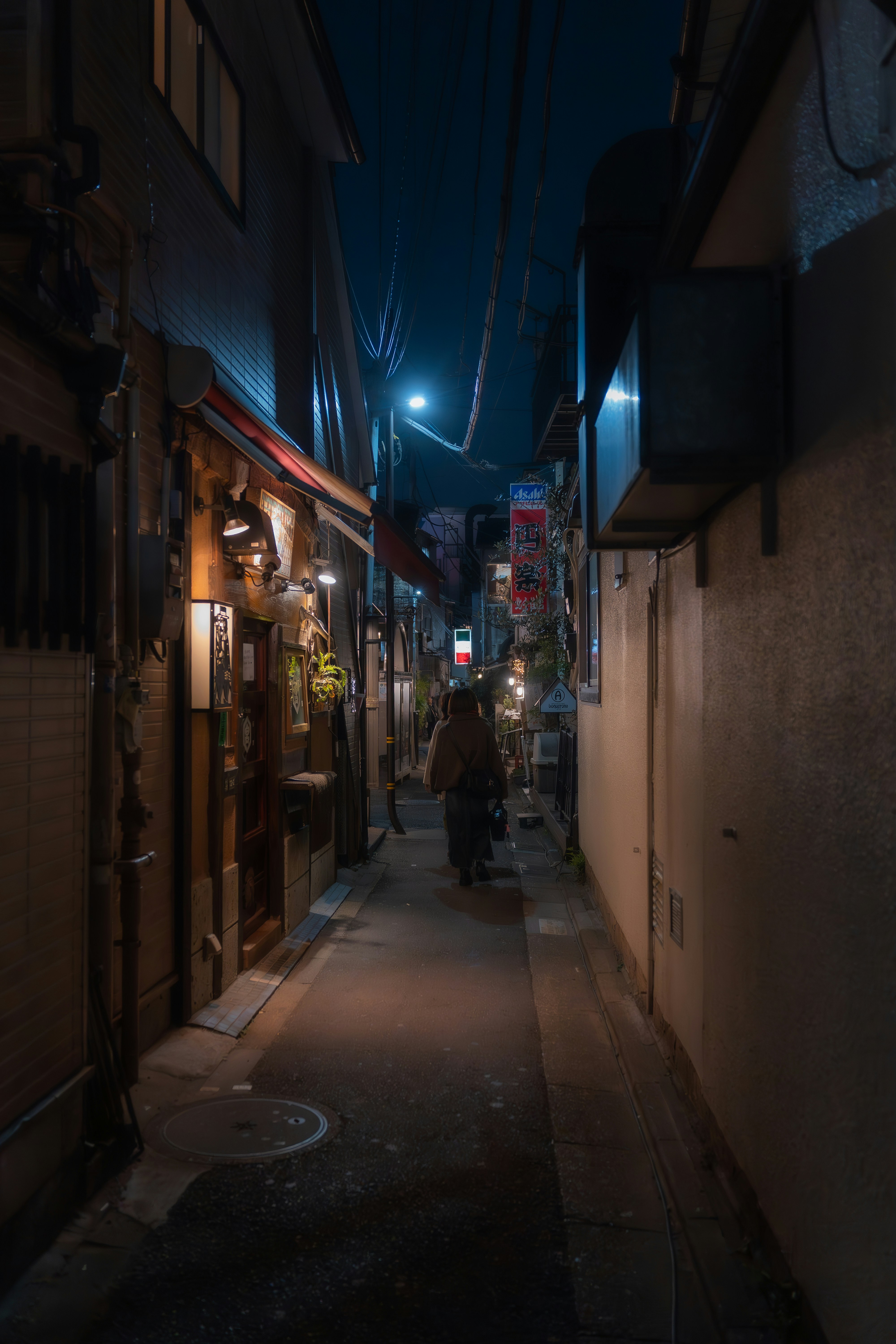 A person walks down a narrow, illuminated alley at night.