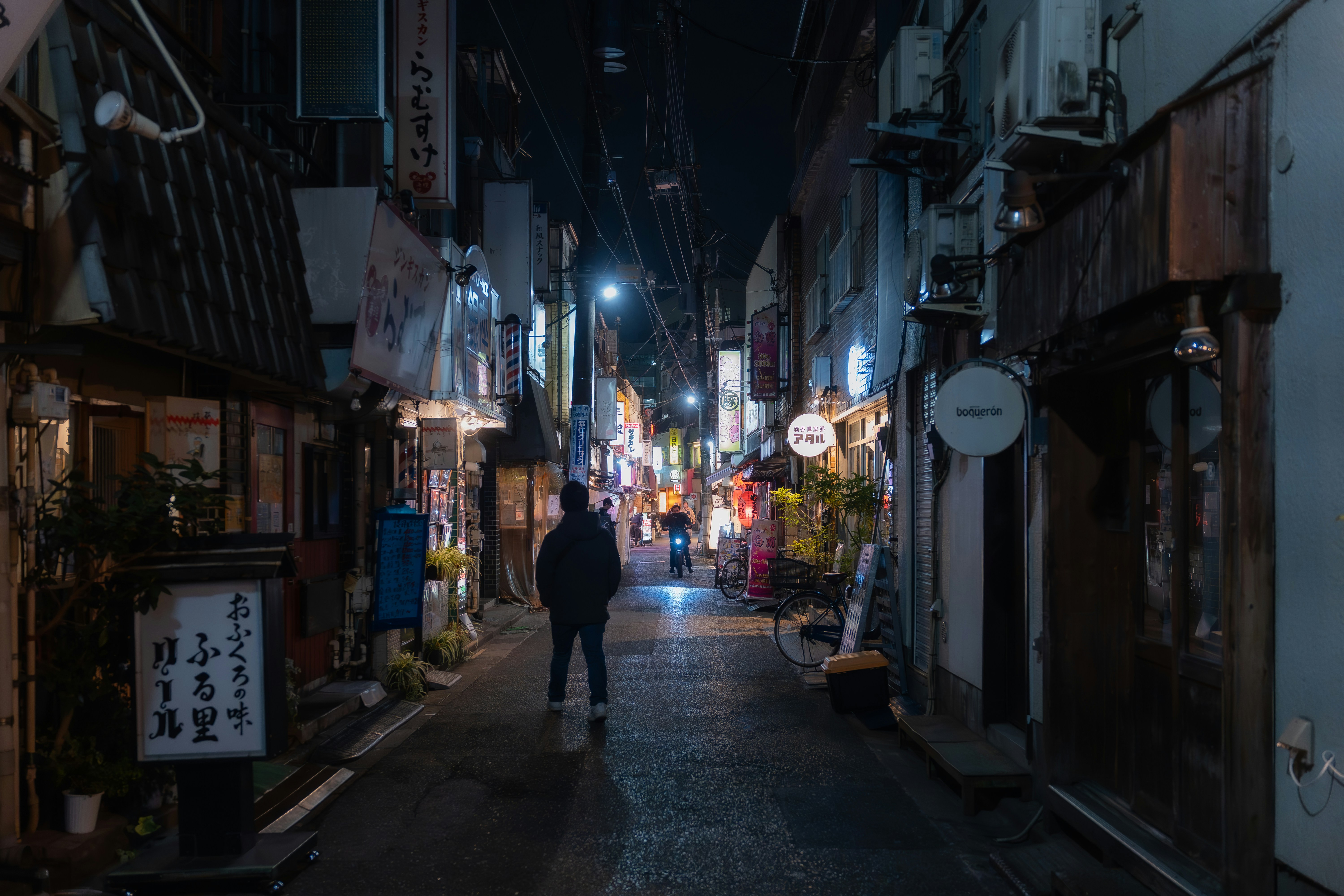 A lone figure walks down a narrow street at night.