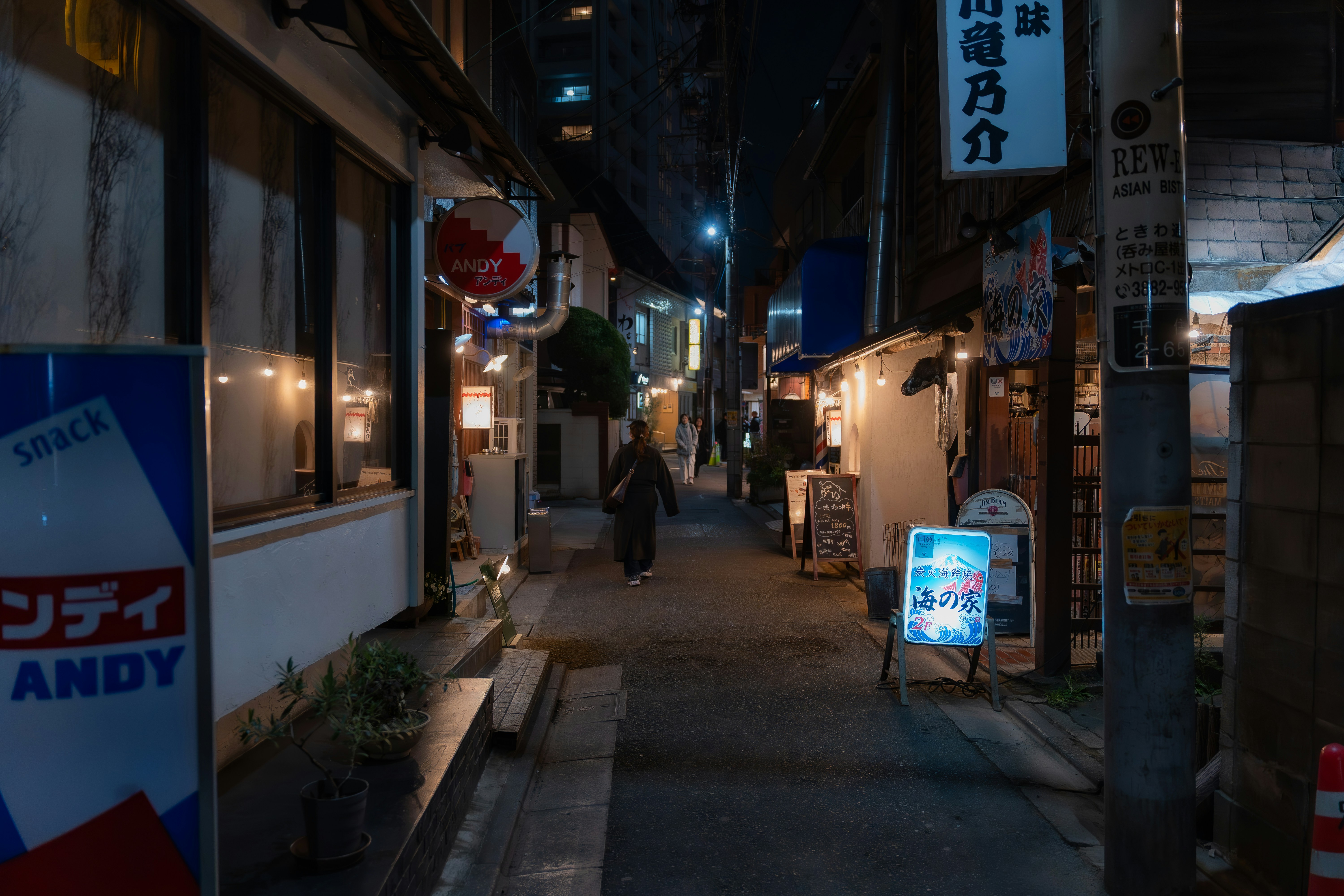 A person walks down a narrow, illuminated alleyway at night.