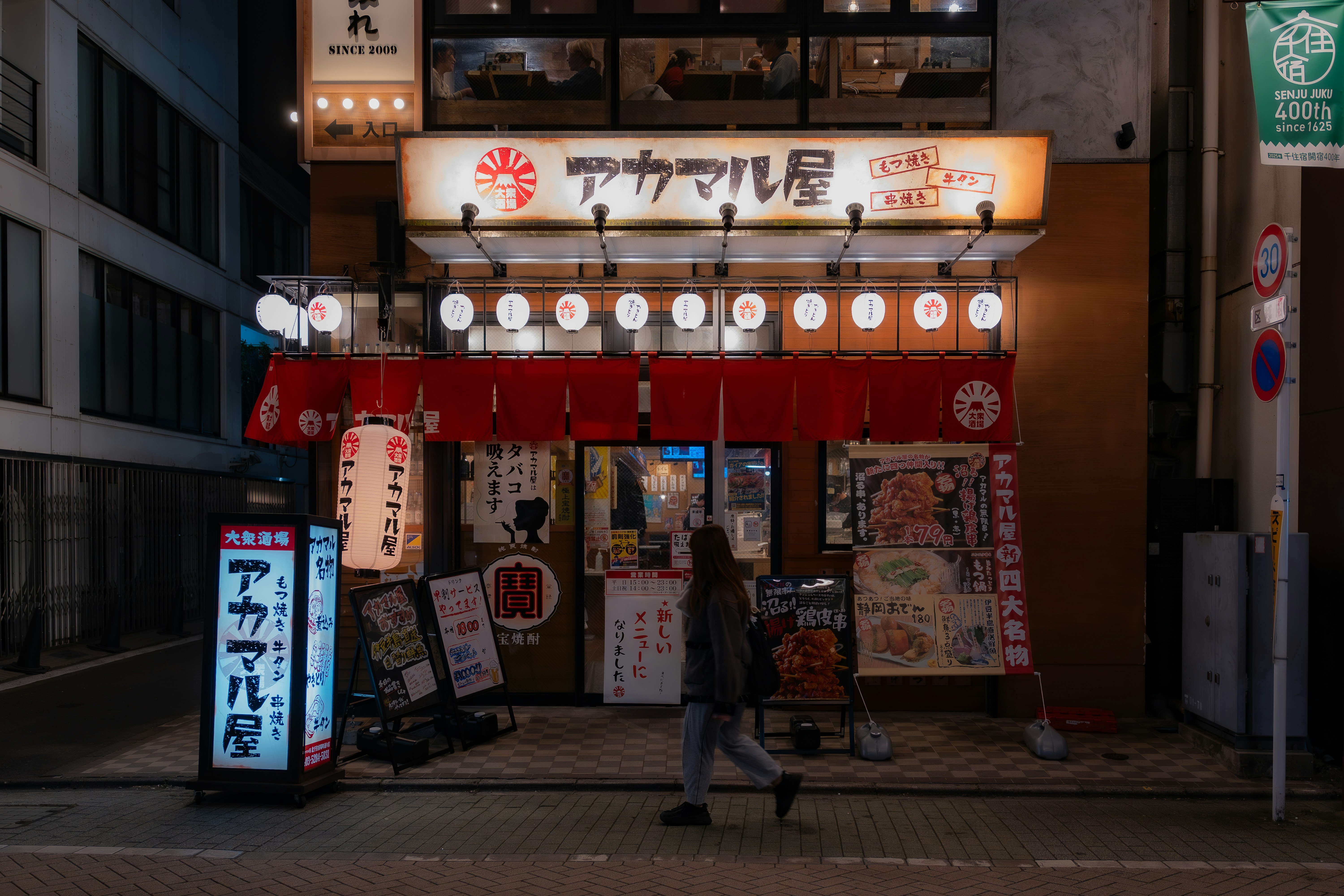 A person walks past a japanese restaurant at night.