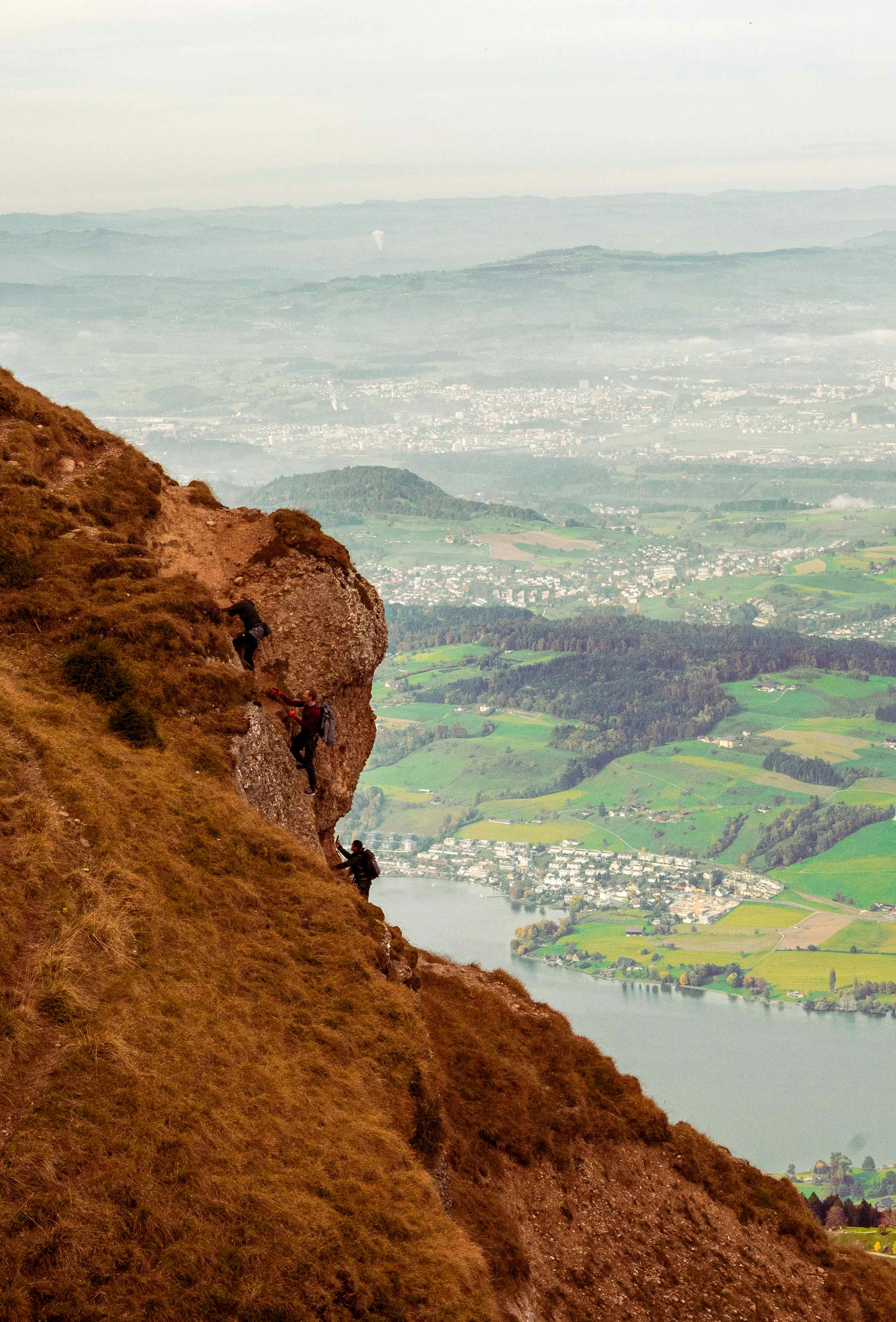 Climbers ascend a rocky mountain slope overlooking a lake.