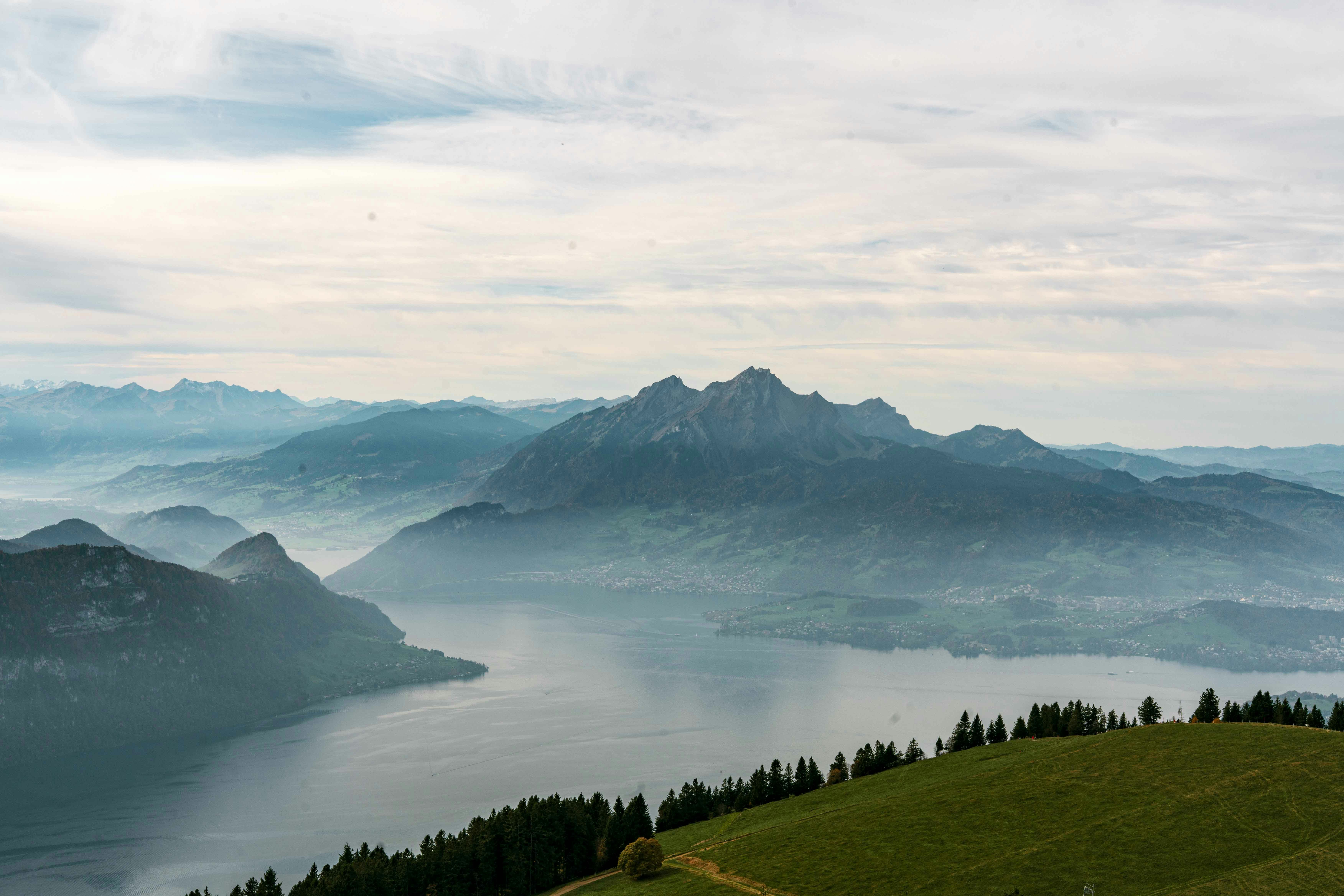 Misty mountains overlook a calm lake with green hills.