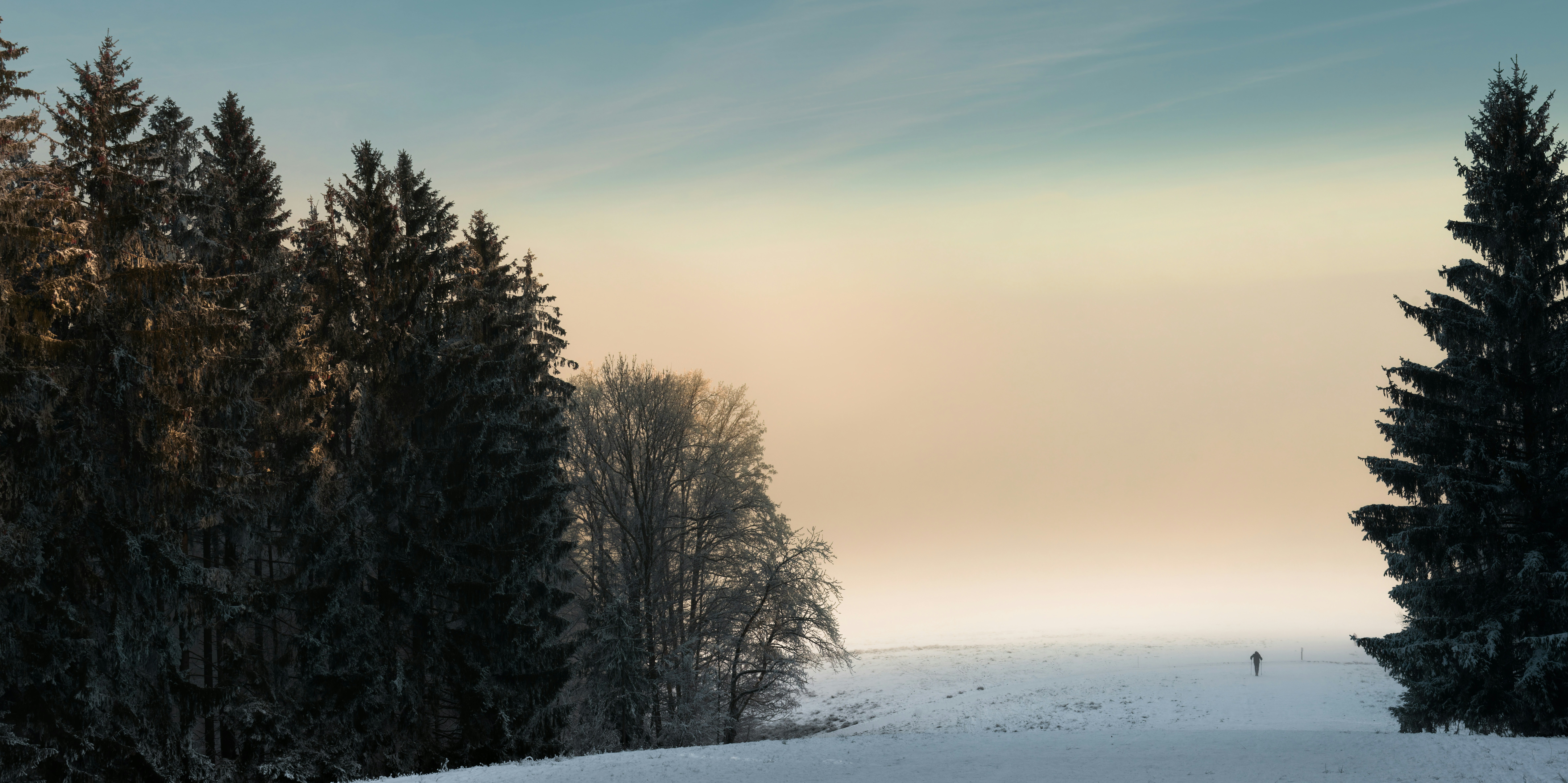 A lone skier traverses a snowy landscape at dusk.
