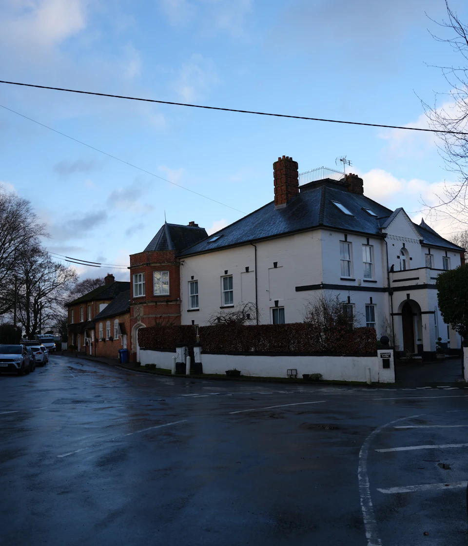 Two-story brick building with white facade and black roof on a street corner exists