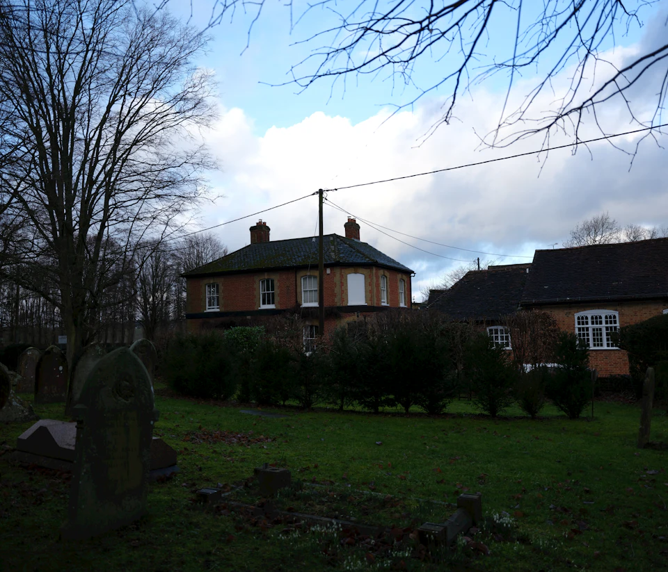 Serene cemetery scene with two houses and a church steeple against an overcast sky backdrop