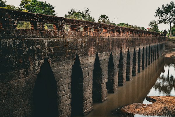 Ancient stone aqueduct with arched openings reflected in water — Kuldīga, Latvia