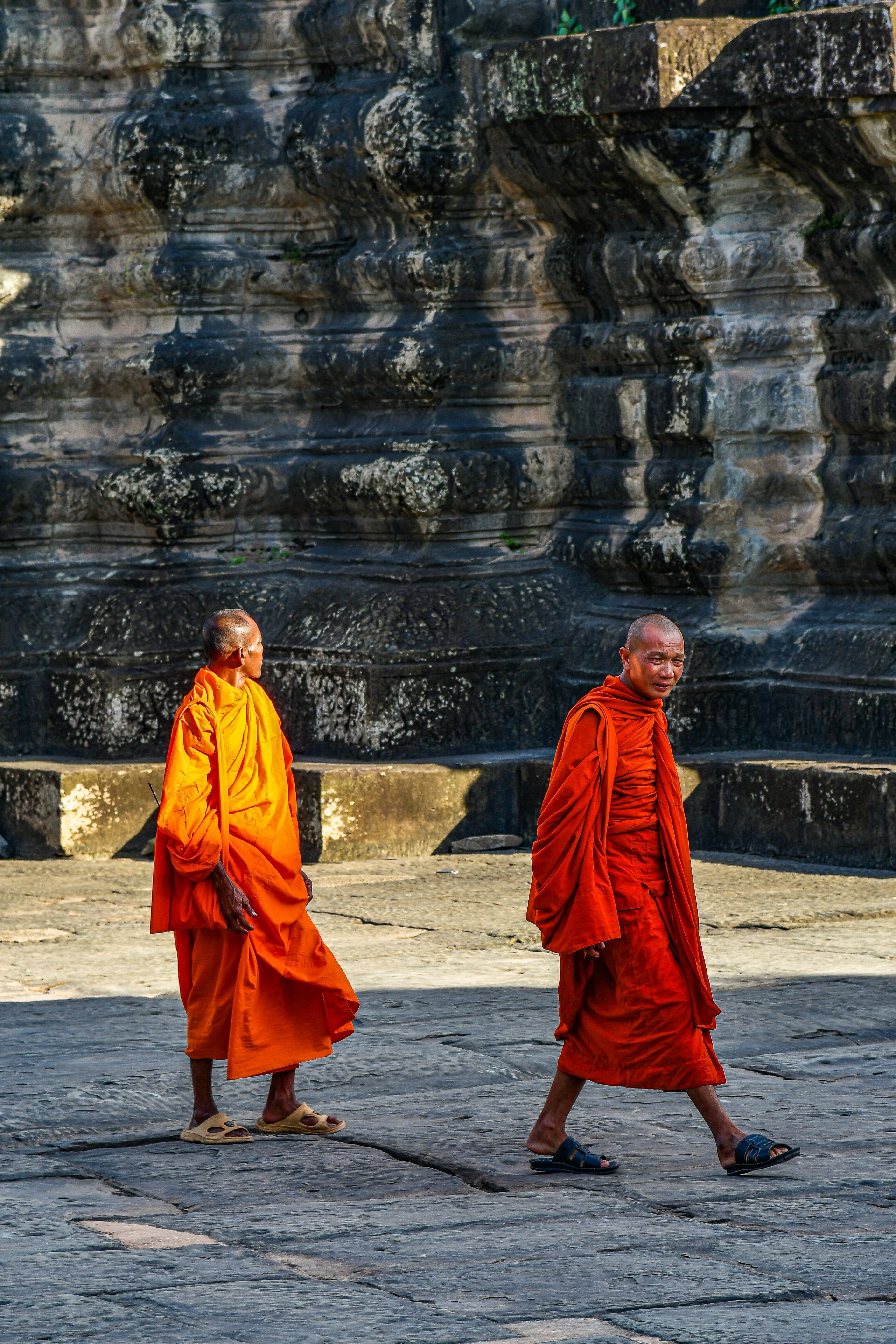 Two buddhist monks in orange robes walk outdoors.