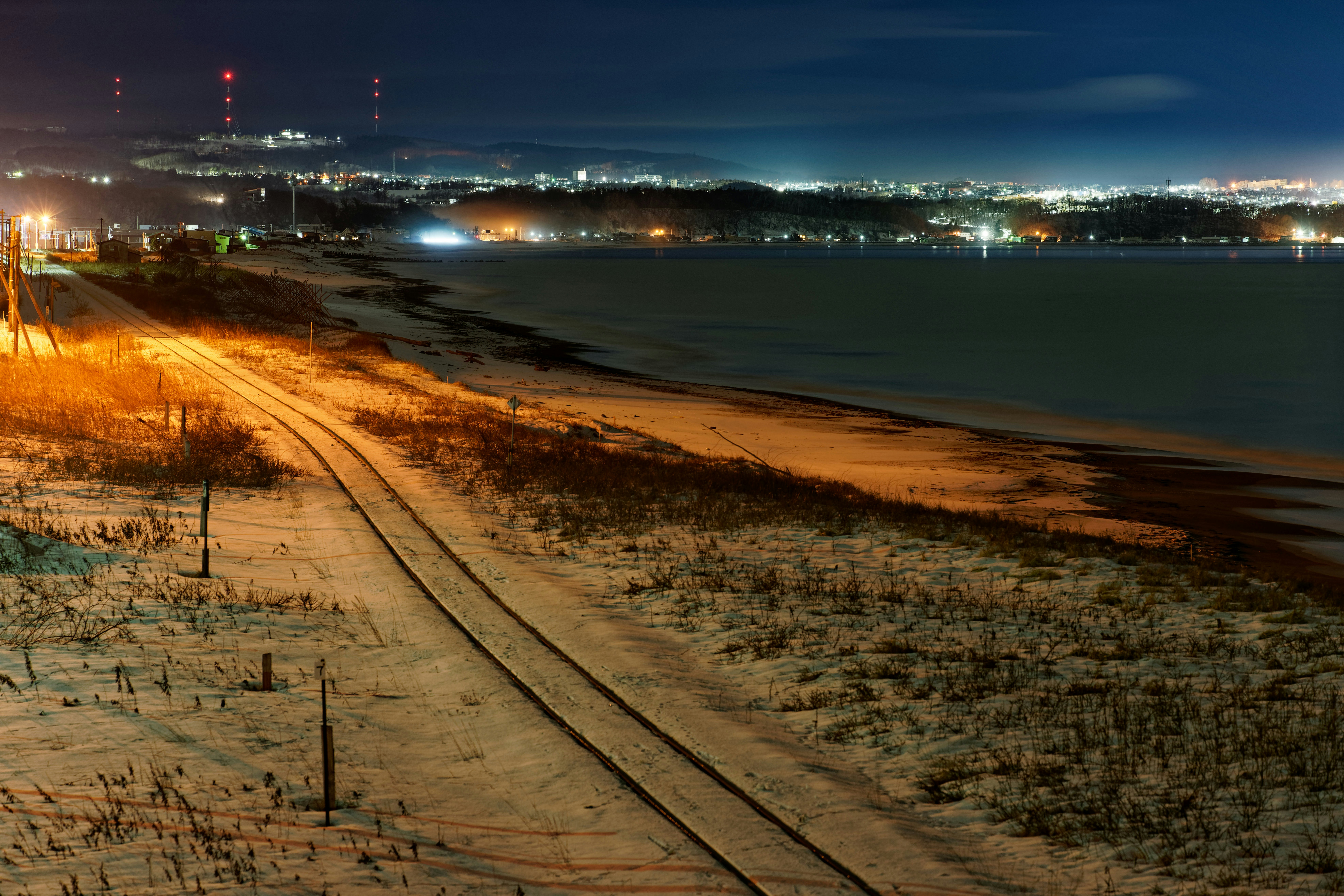 Snowy train tracks lead towards a distant city at night.