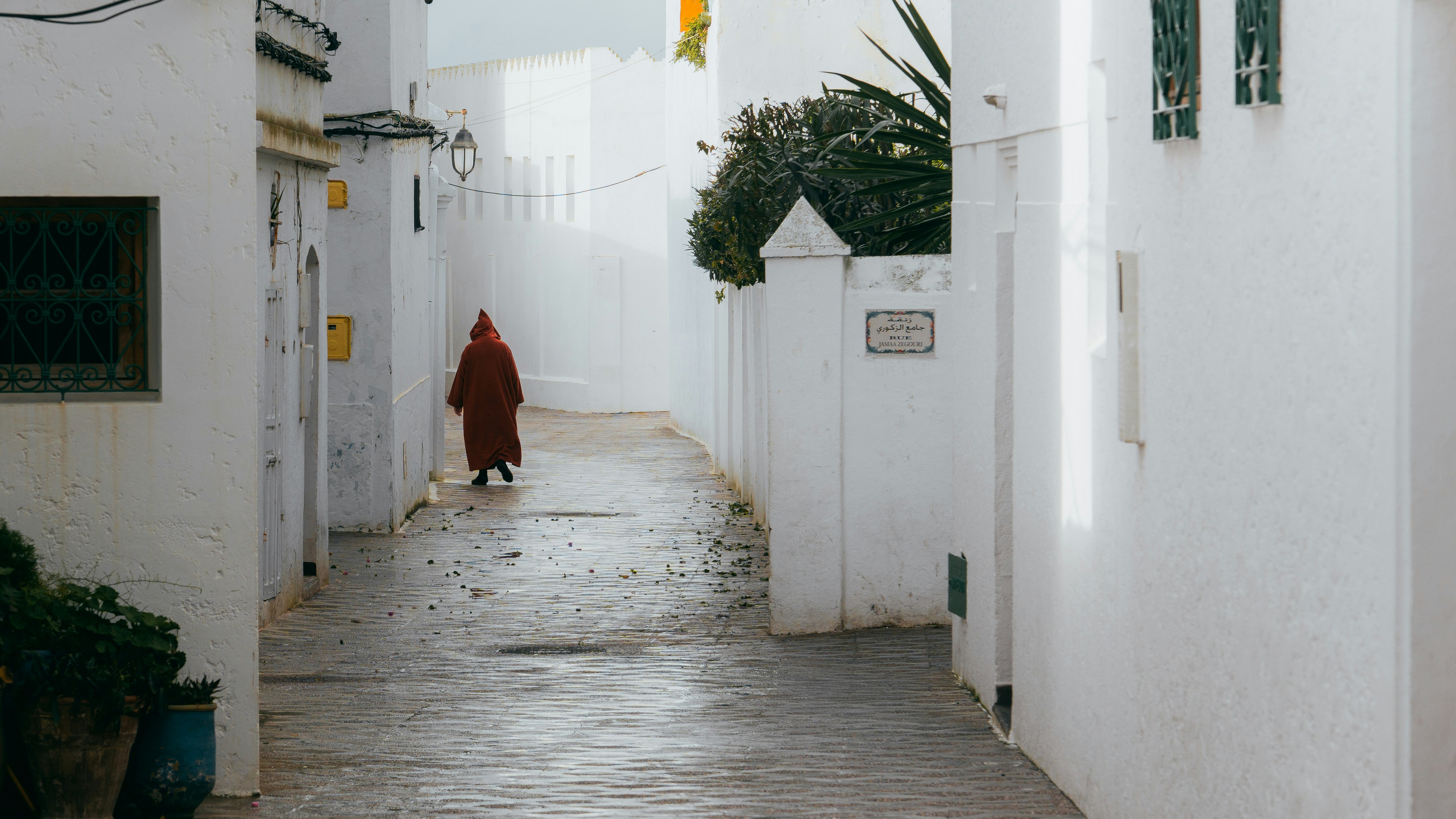 Person in red robe walks down narrow white alleyway.