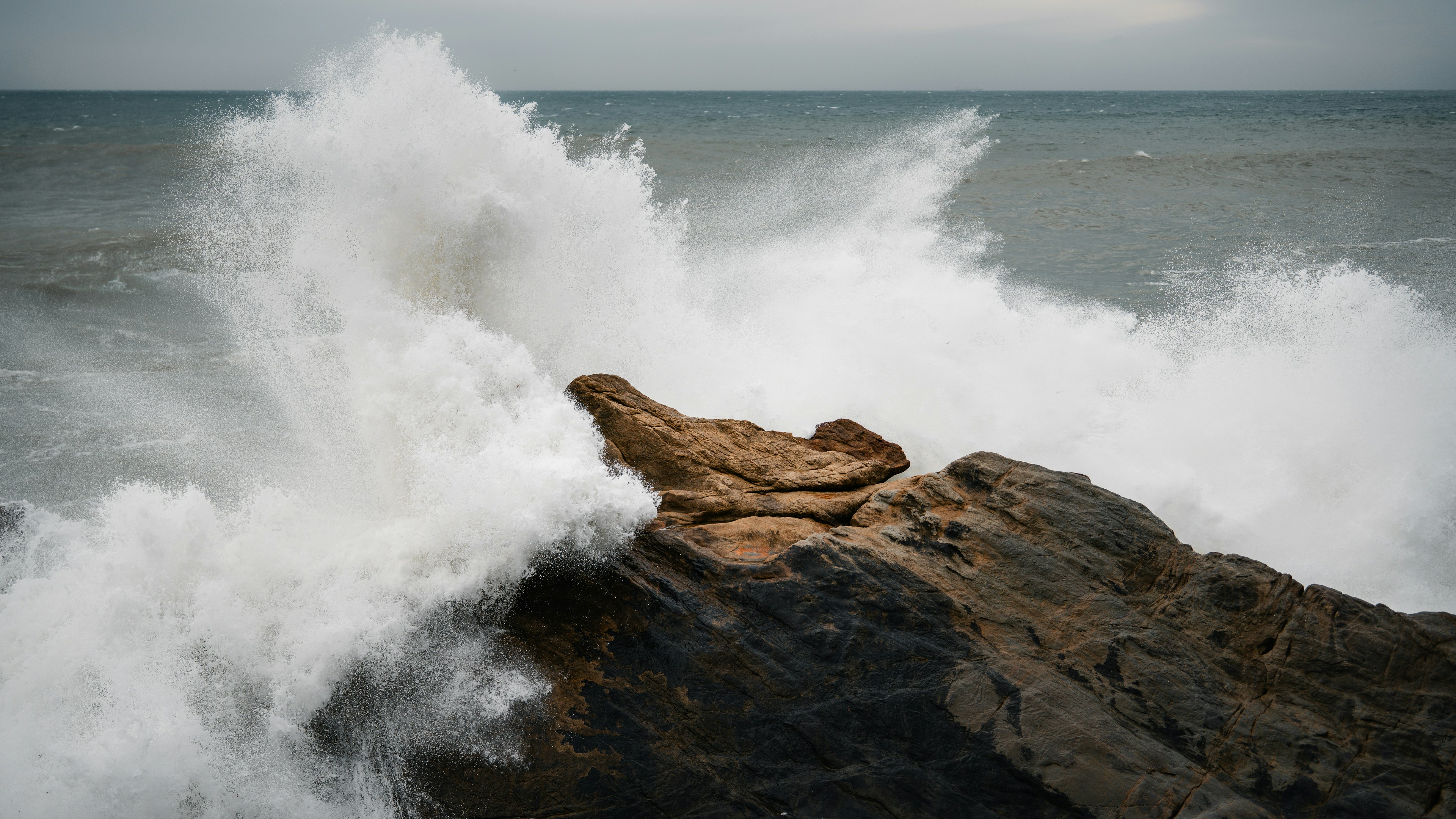 흐린 하늘 아래 바위 해안선에 부서지는 파도
