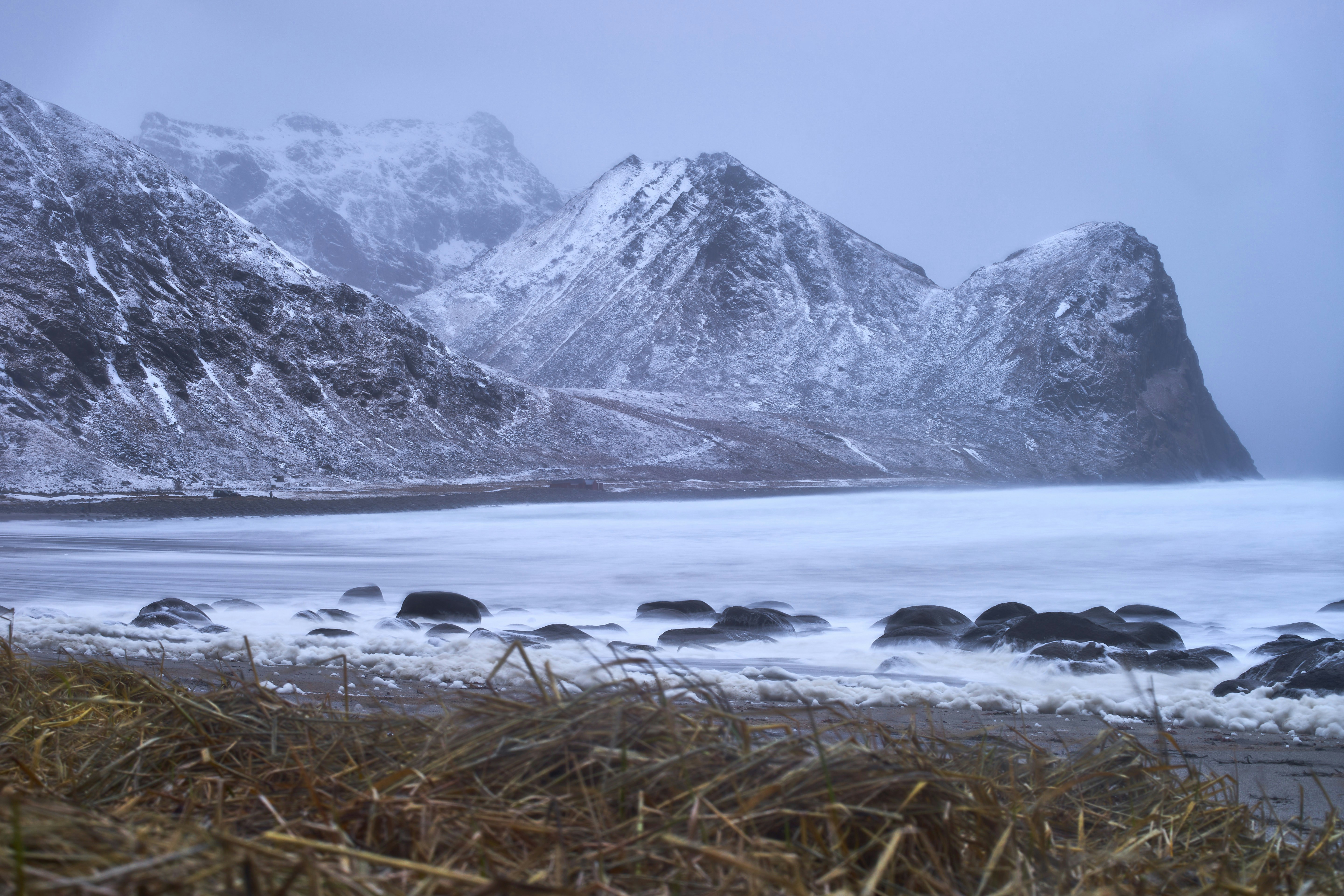 Snowy mountains overlooking a frozen beach with rocks.