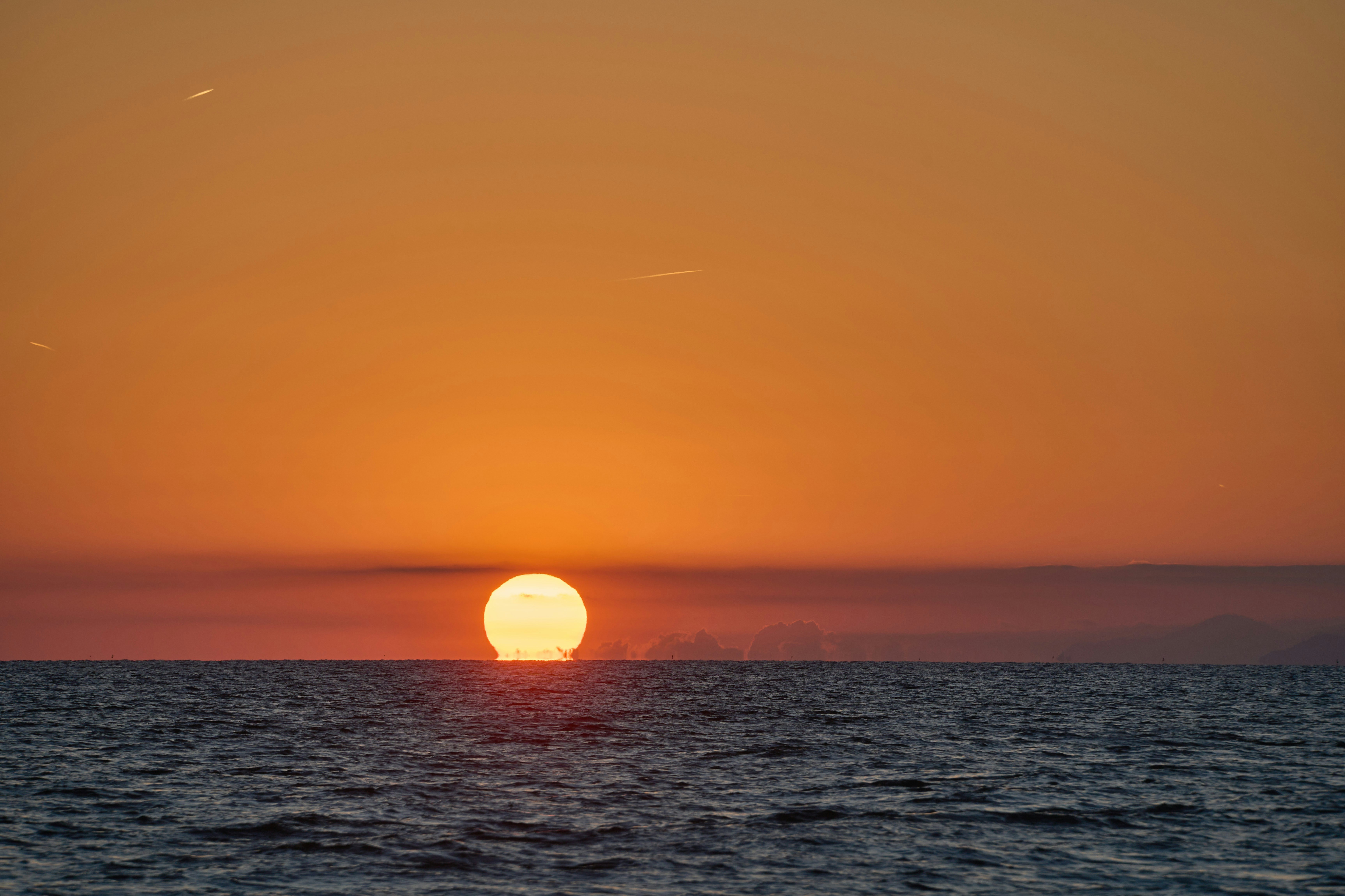 The sun sets over a calm ocean horizon.