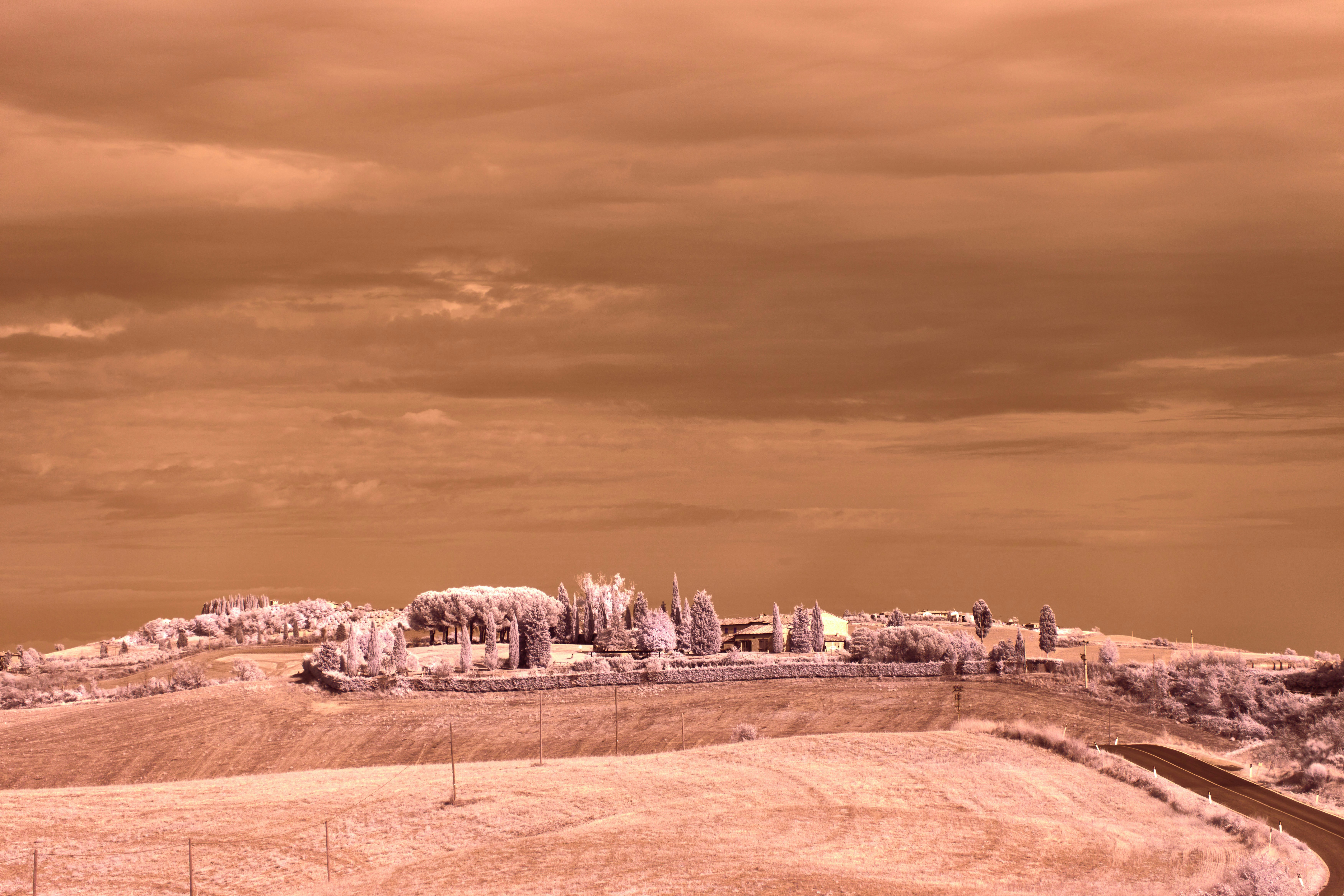 Rural landscape with buildings on a hill under cloudy sky.