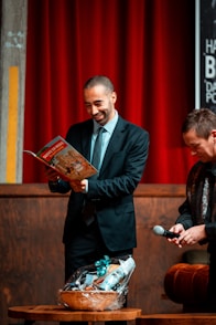 Man in suit reads magazine, gift basket nearby.