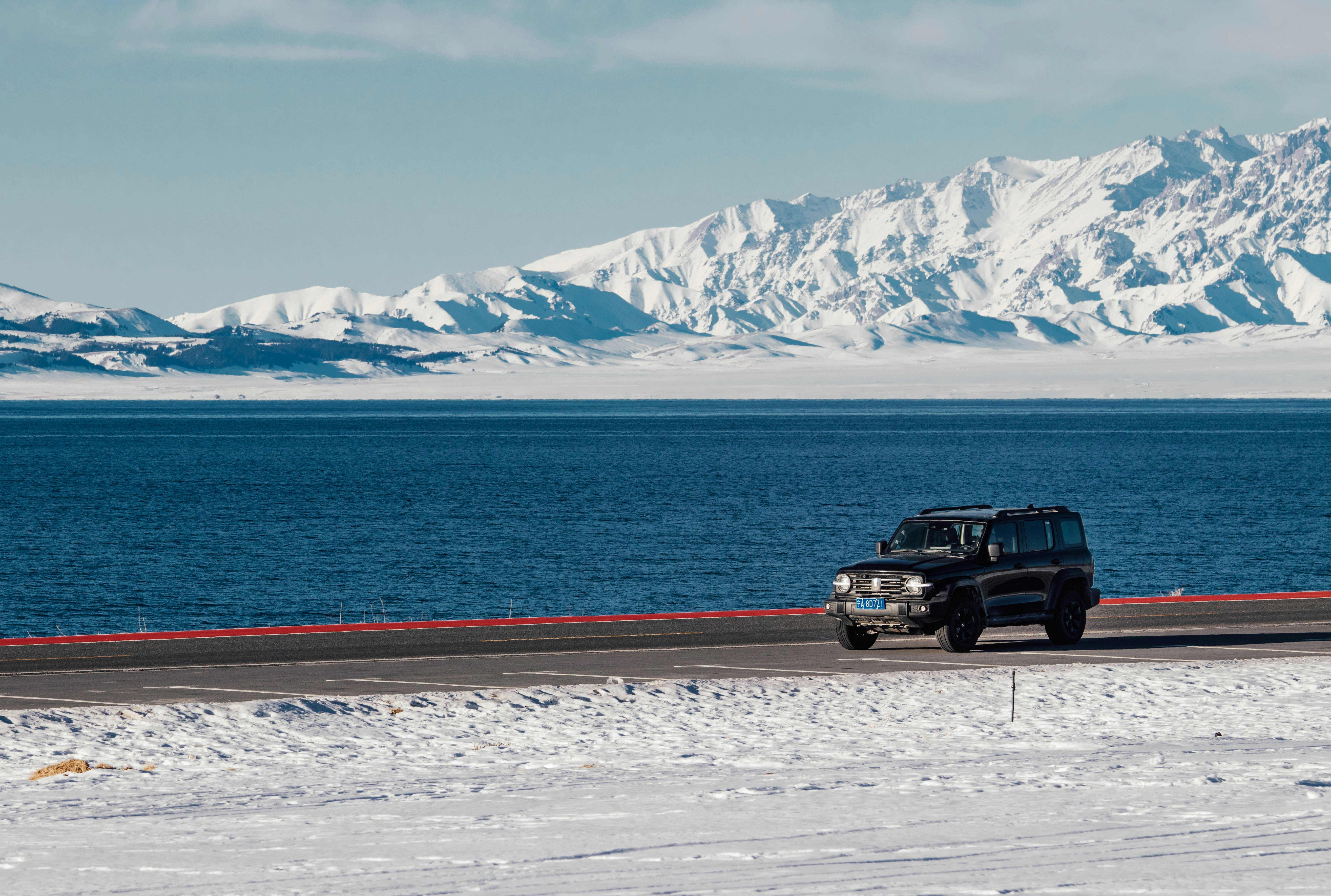 Black suv driving on a road by a snowy lake.