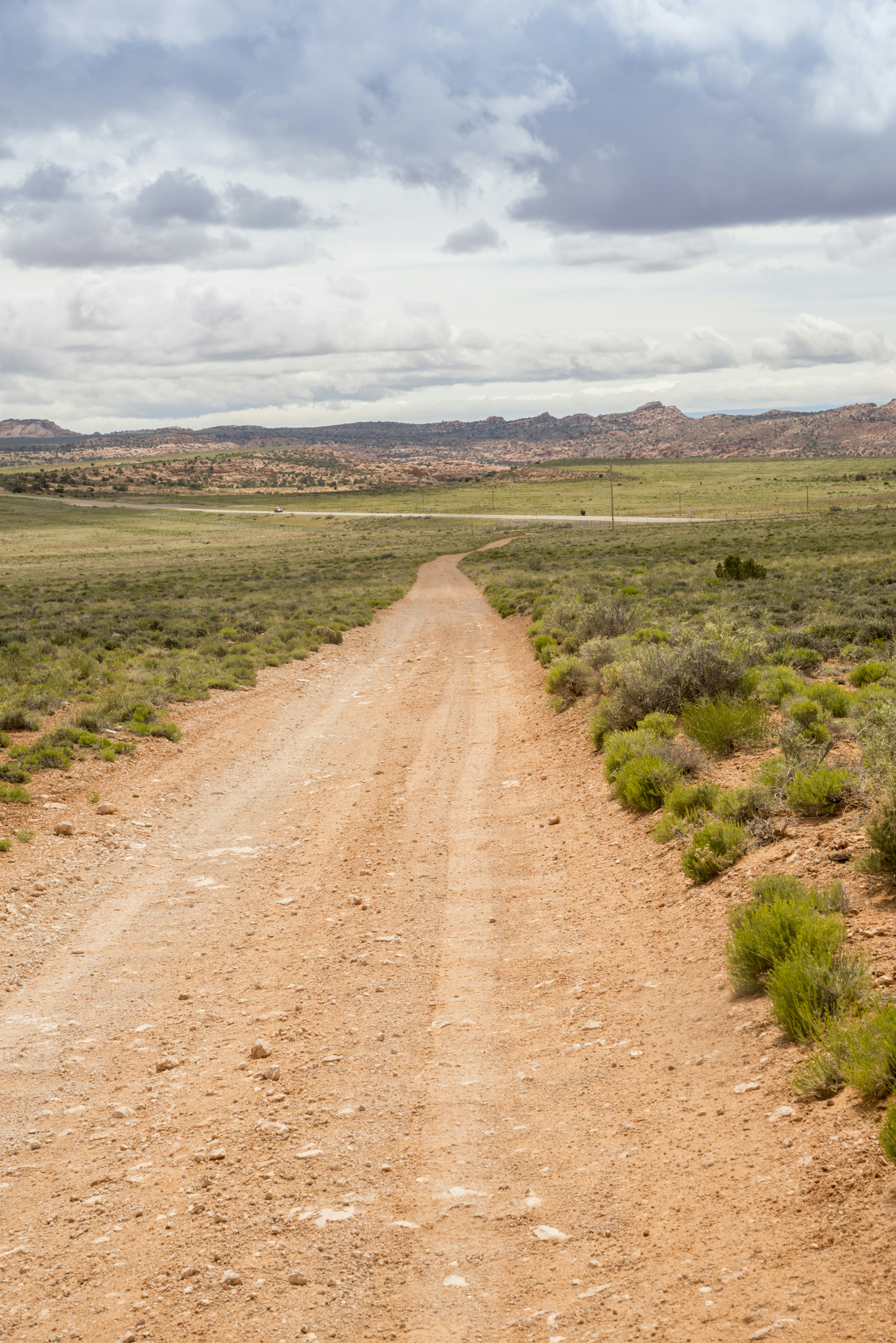 A long dirt road creates strong leading lines through an open desert landscape, extending toward distant mountains beneath a wide sky with ample copy space.