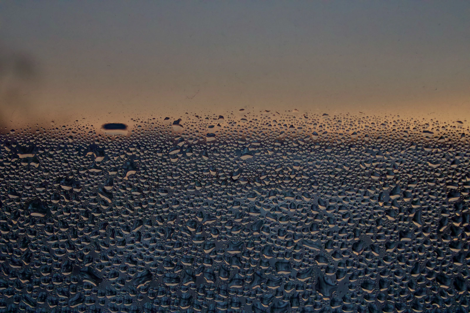 Water droplets on glass against an evening sky