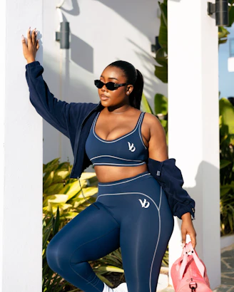 A woman in navy activewear holds a pink gym bag.