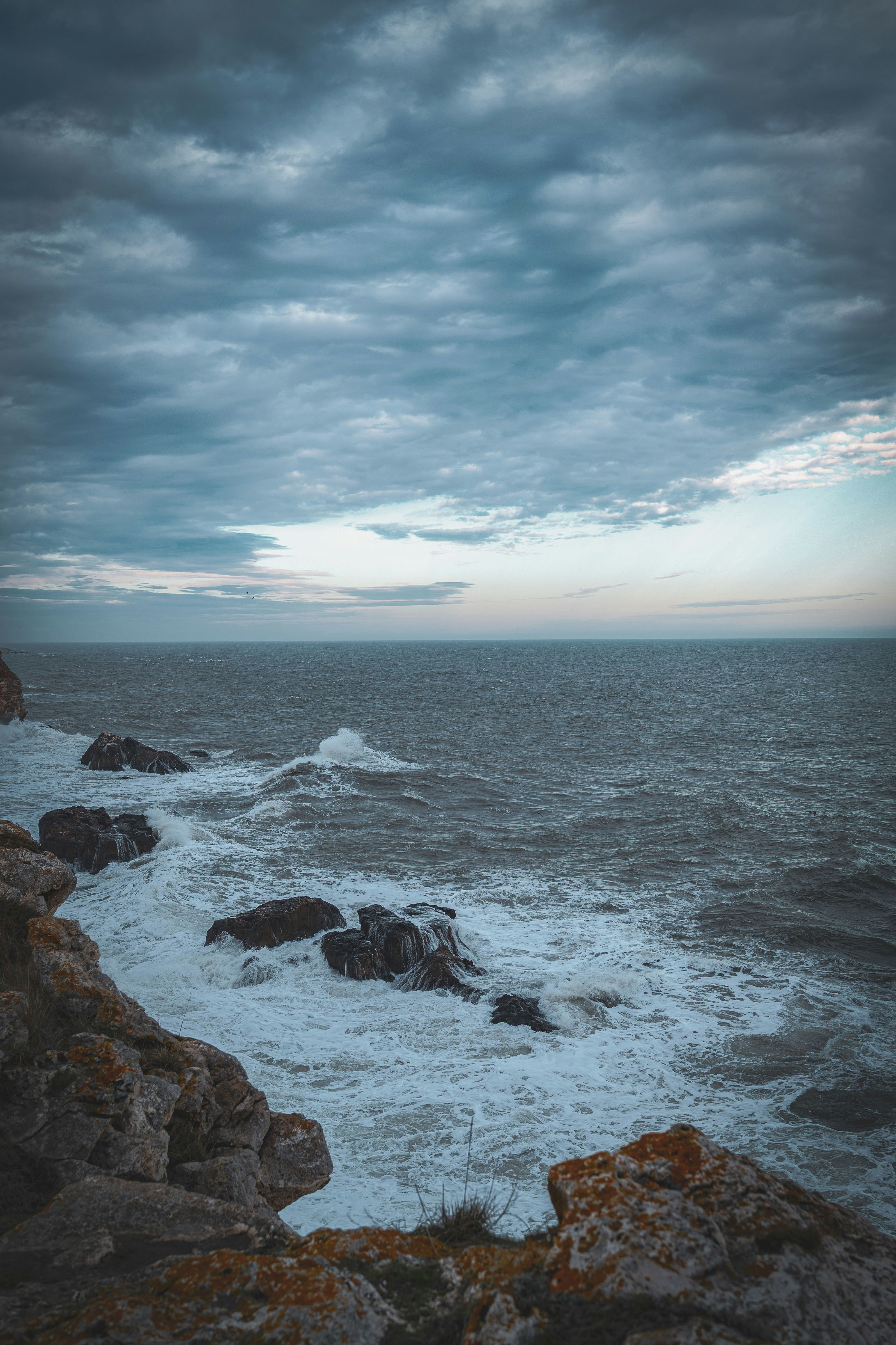 Wellen, die unter bewölktem Himmel gegen das felsige Ufer schlagen