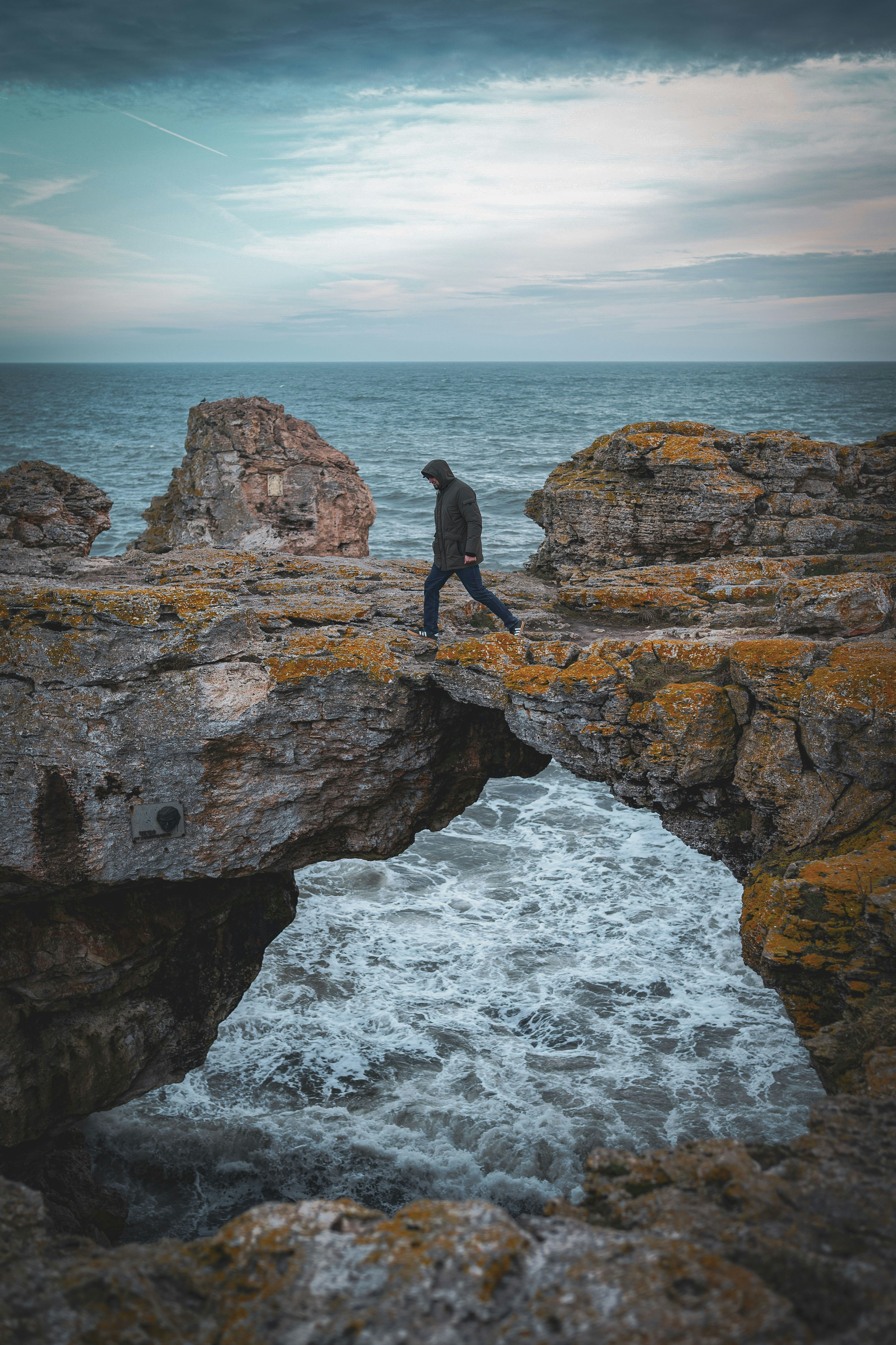 Mann geht über felsigen Bogen über tosende Wellen