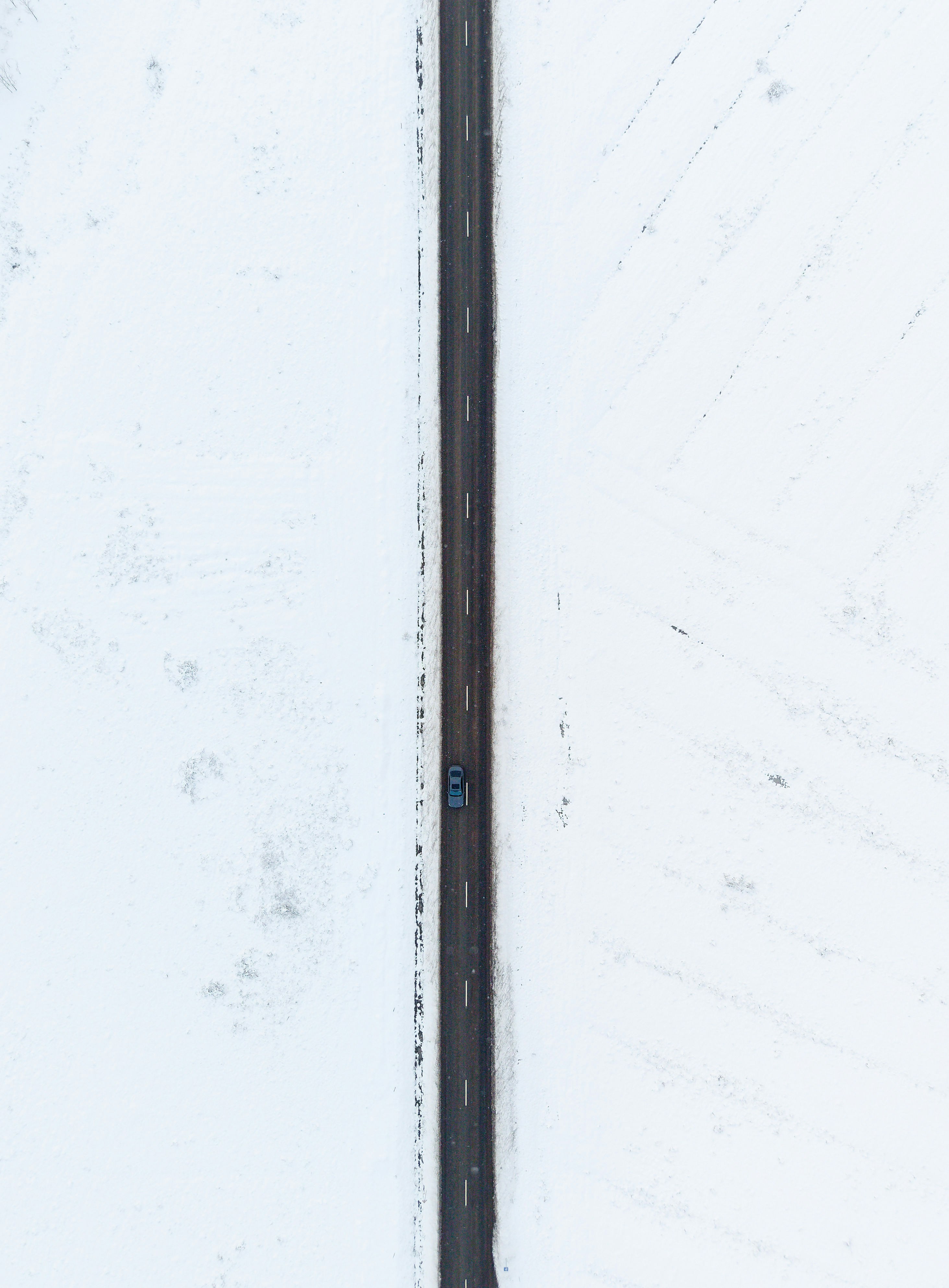 A car drives down a snowy road from above