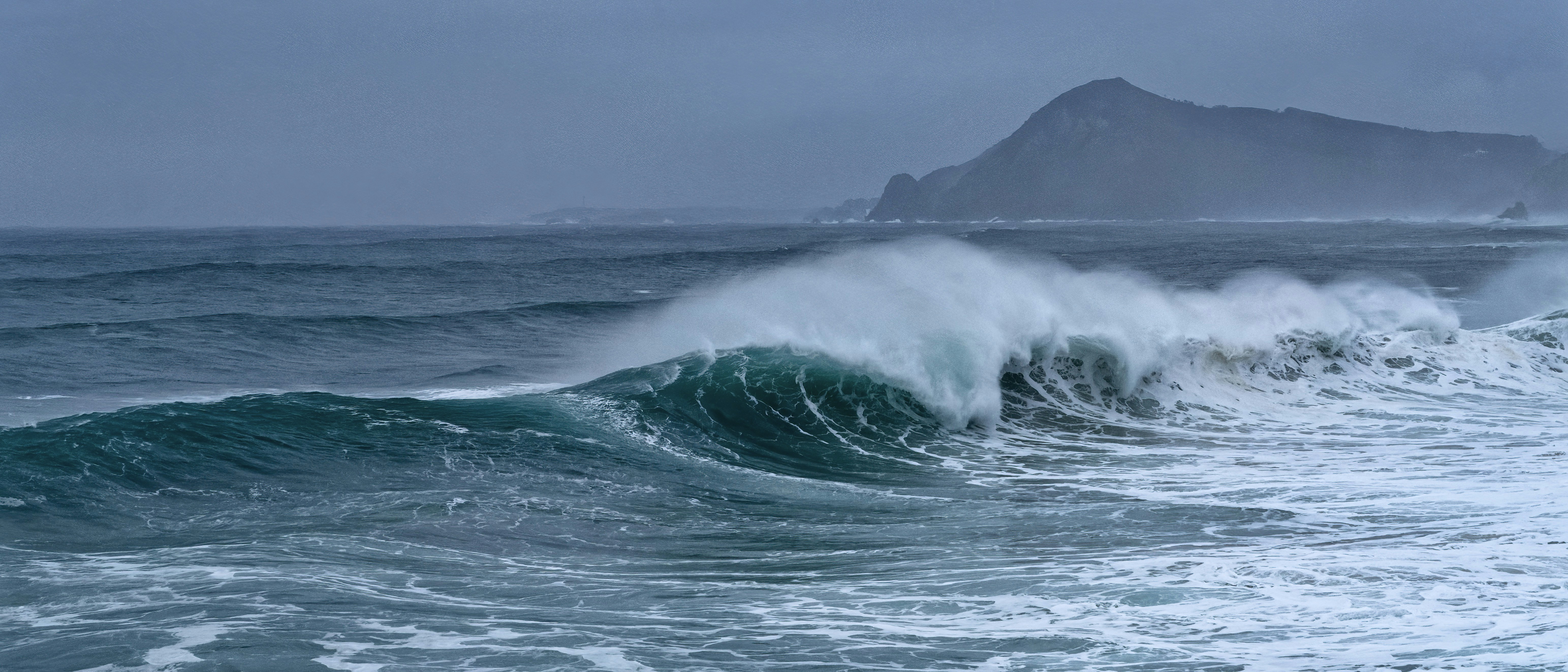 A large wave crashes on a stormy ocean day.