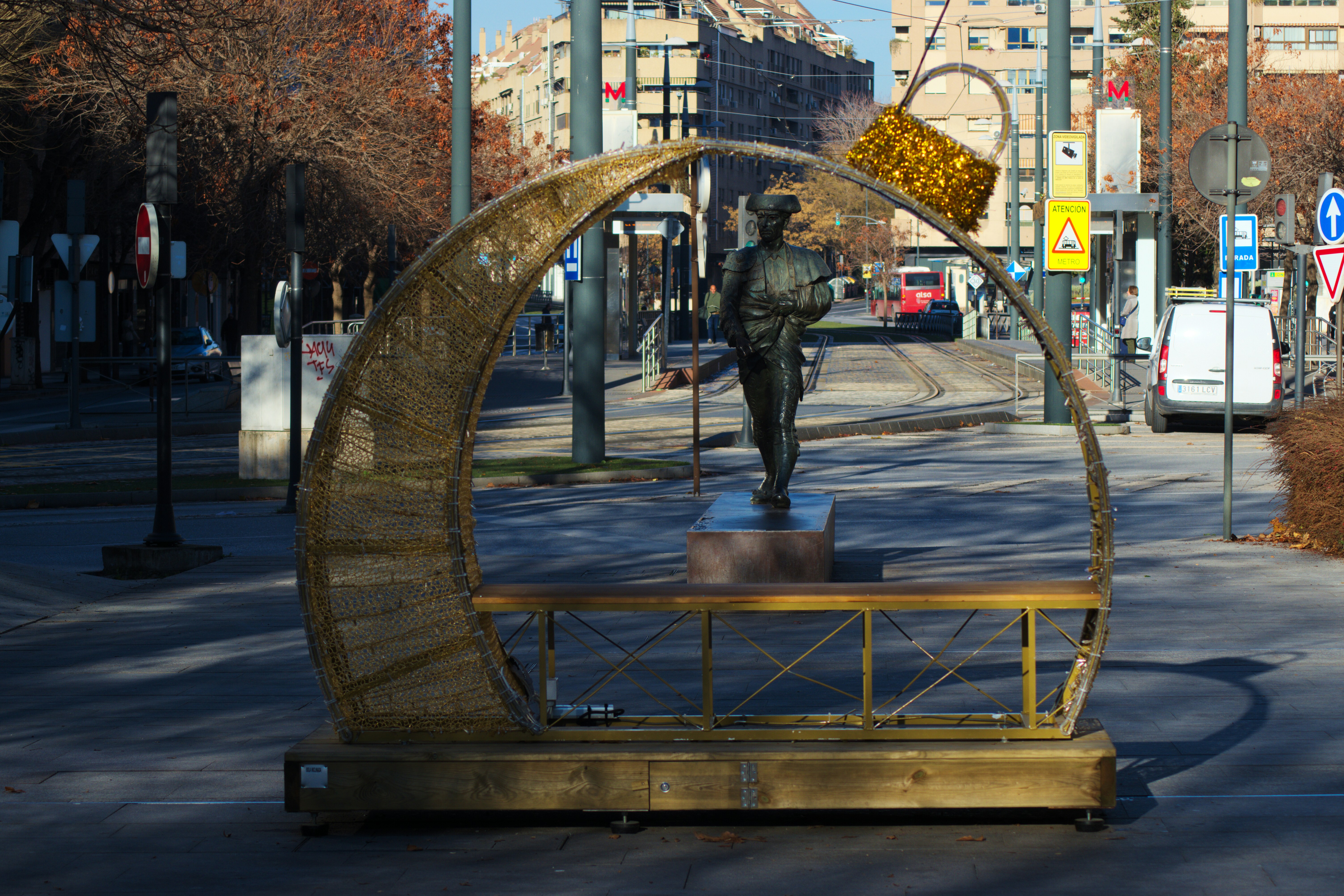 Escultura con una estatua y un banco en una calle.