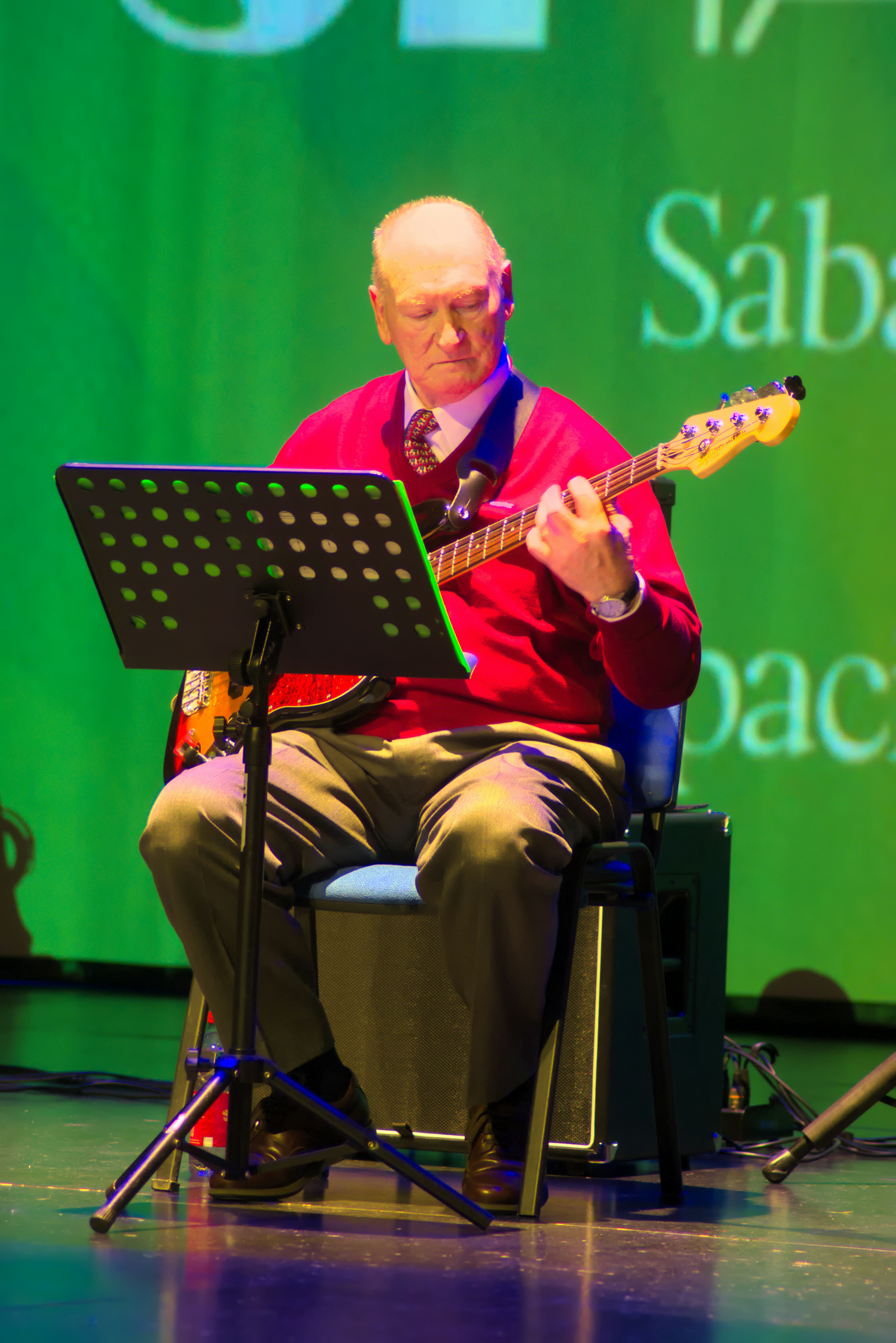 An older man plays a bass guitar on stage.