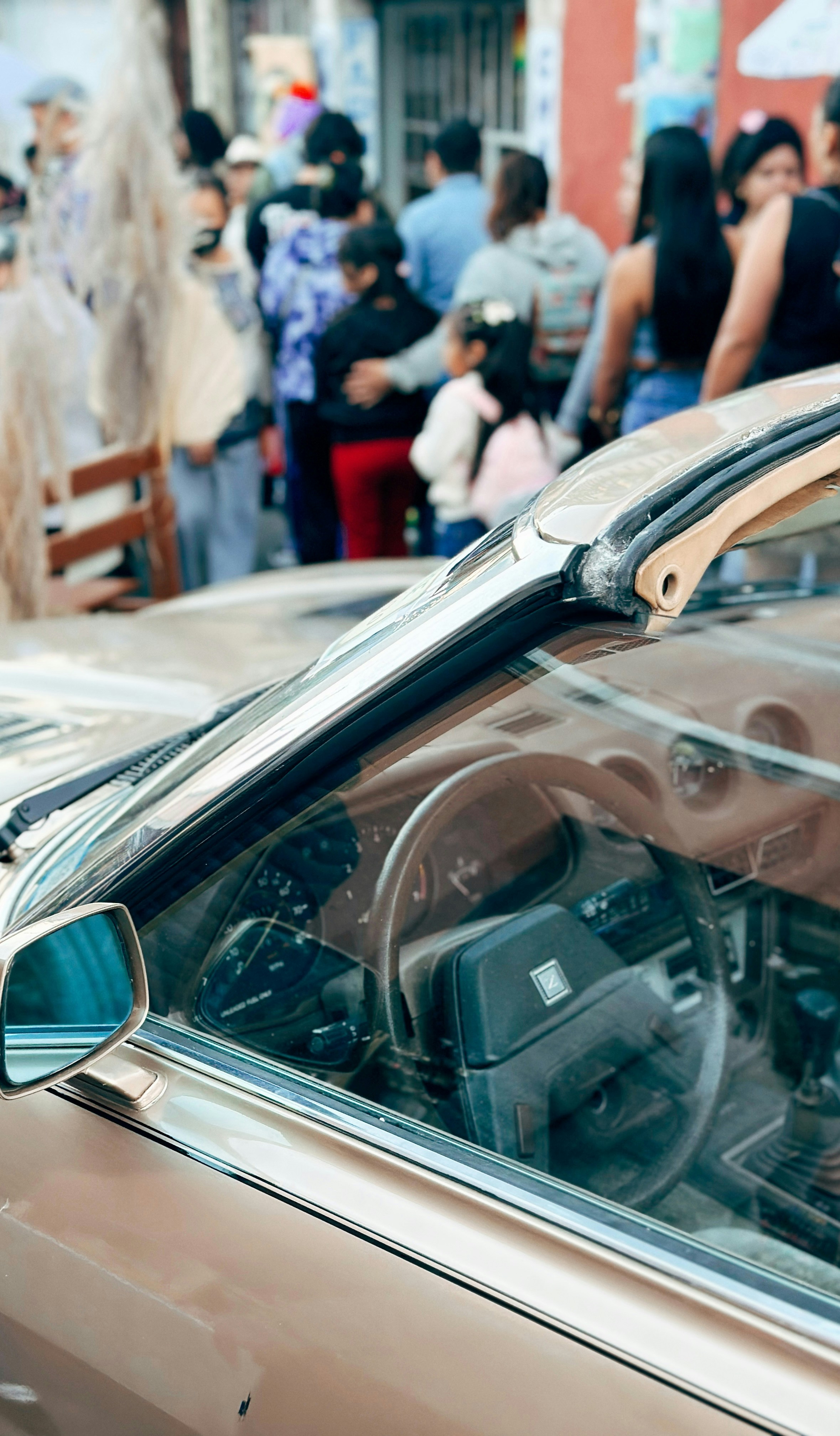 Close-up of a vintage car's interior with people blurred behind.