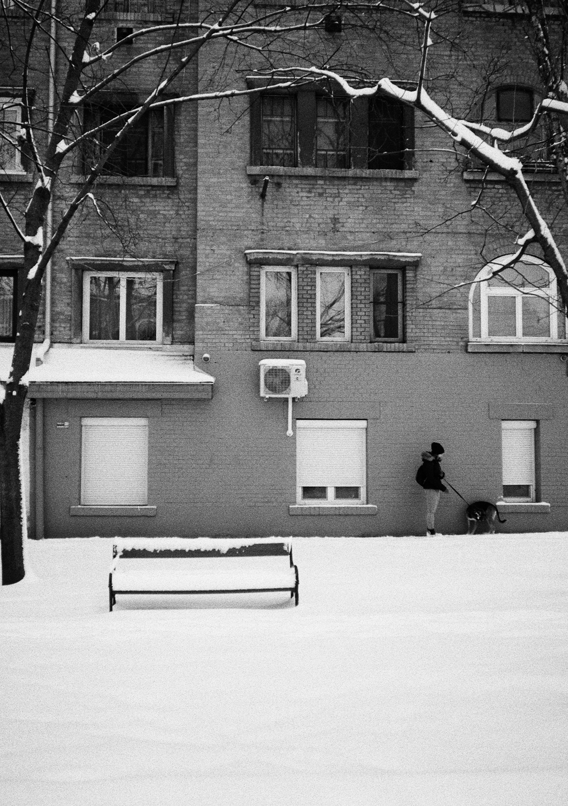 A person shovels snow in front of a brick building.