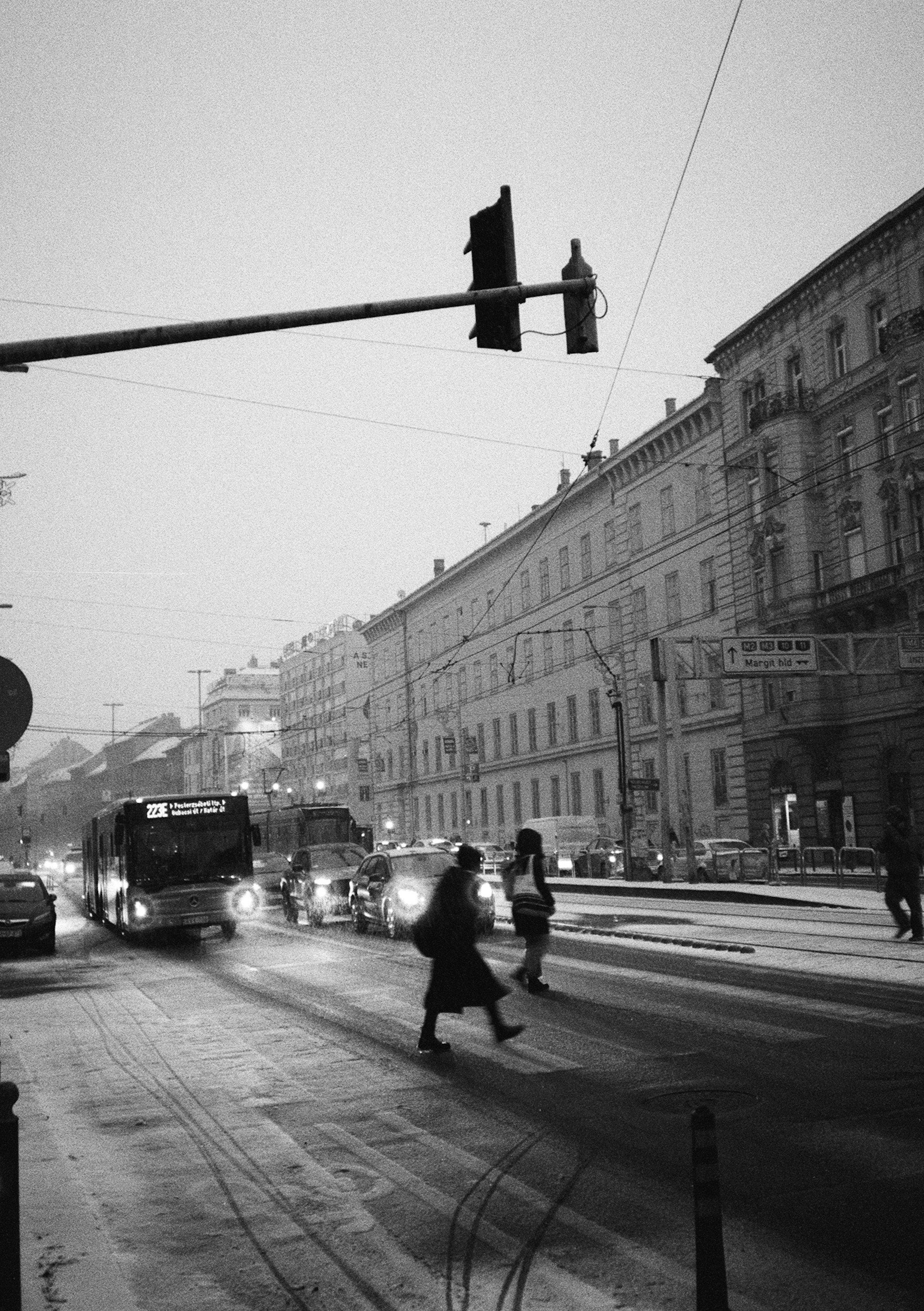 Menschen, die eine verschneite Stadtstraße mit Verkehr überqueren.