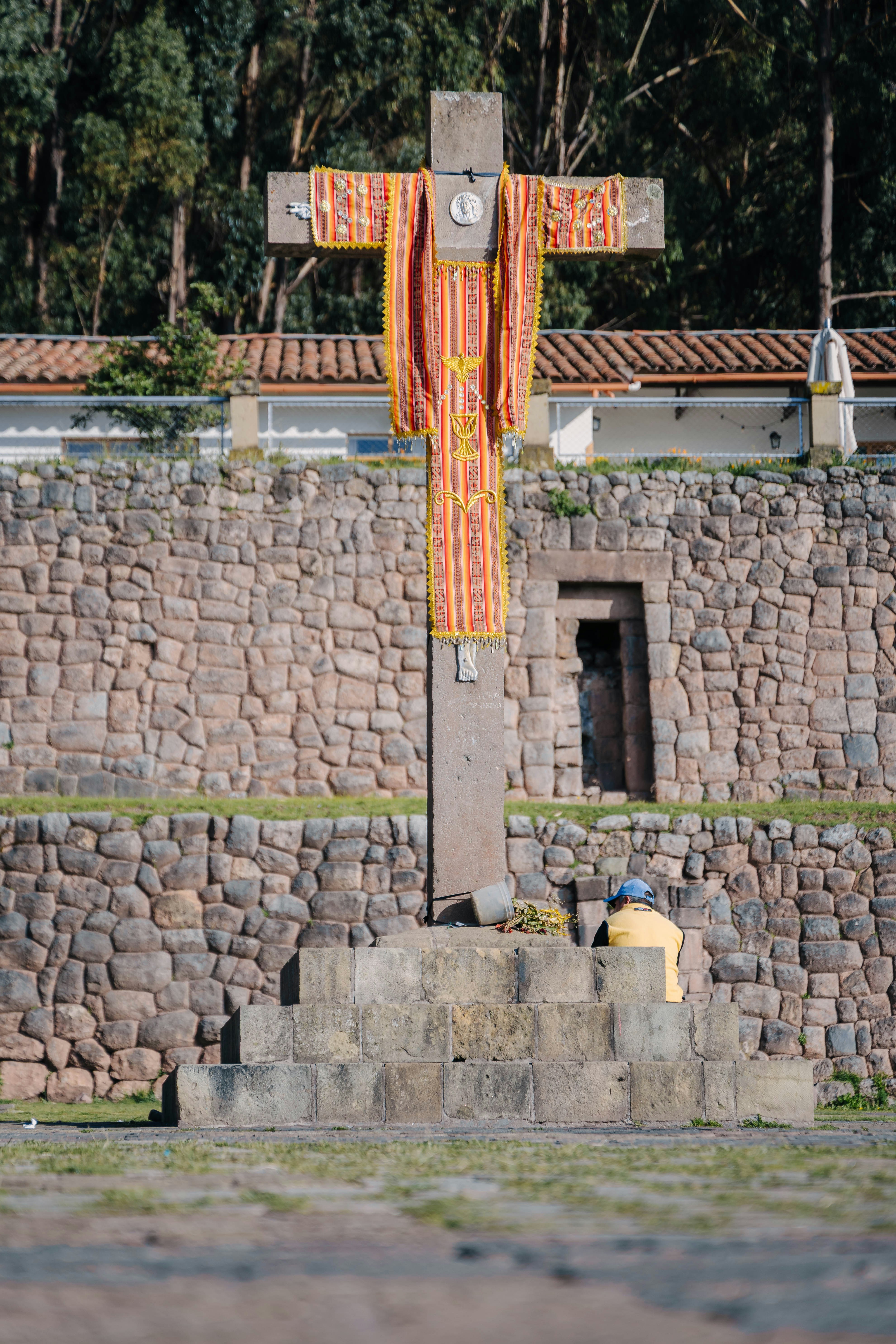 Stone cross with ornate fabric and a person kneeling.
