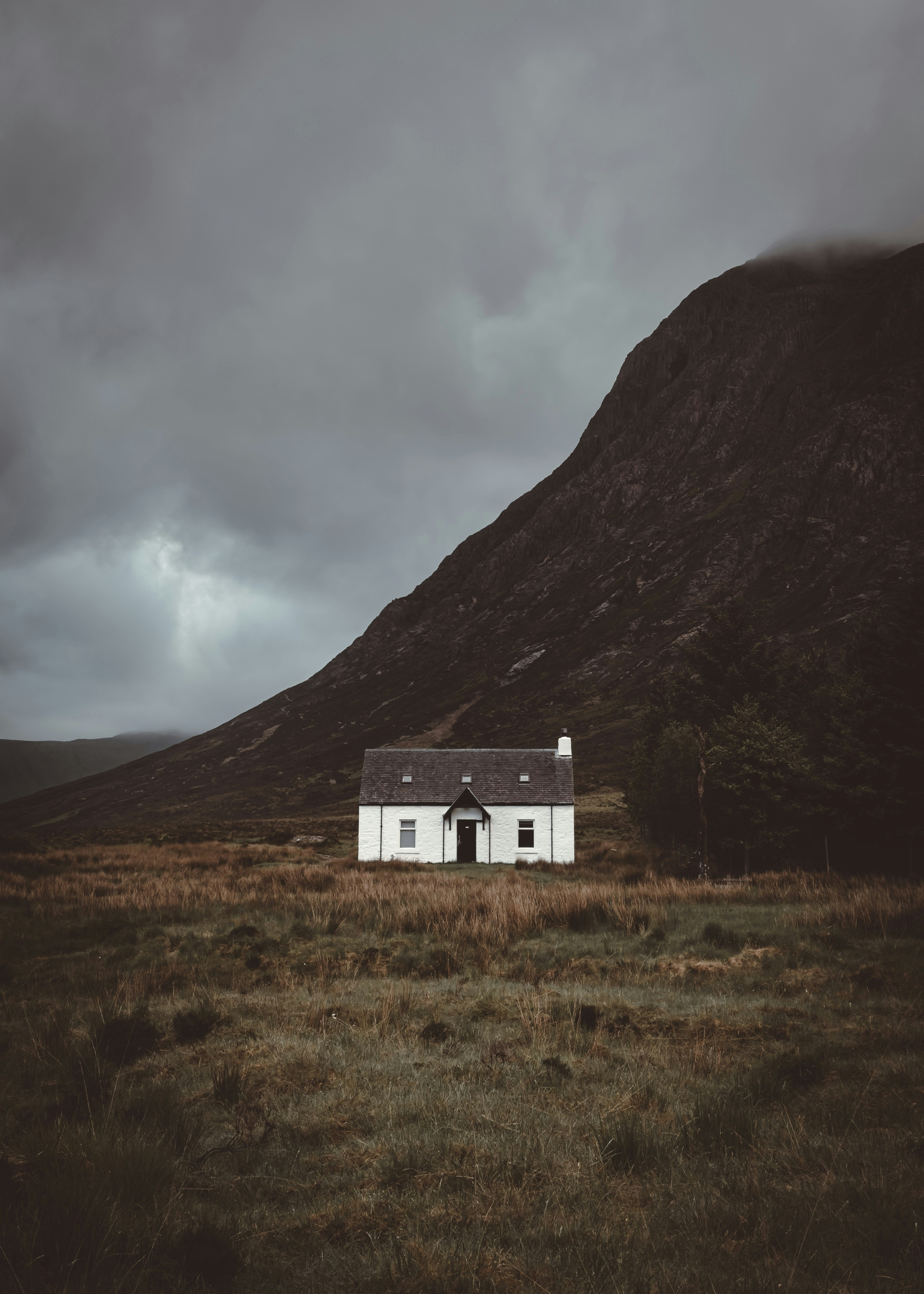 A solitary white house stands against a moody mountain backdrop.