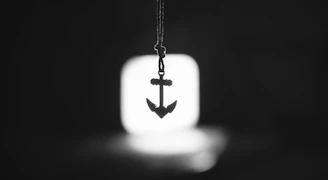 A silver anchor pendant hanging in front of a light.