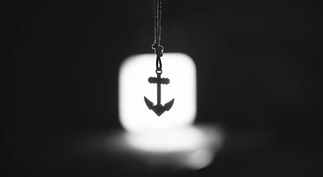 A silver anchor pendant hanging in front of a light.