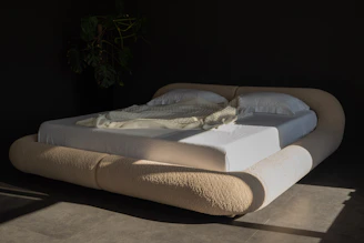 Modern bed with rounded headboard and white linens.