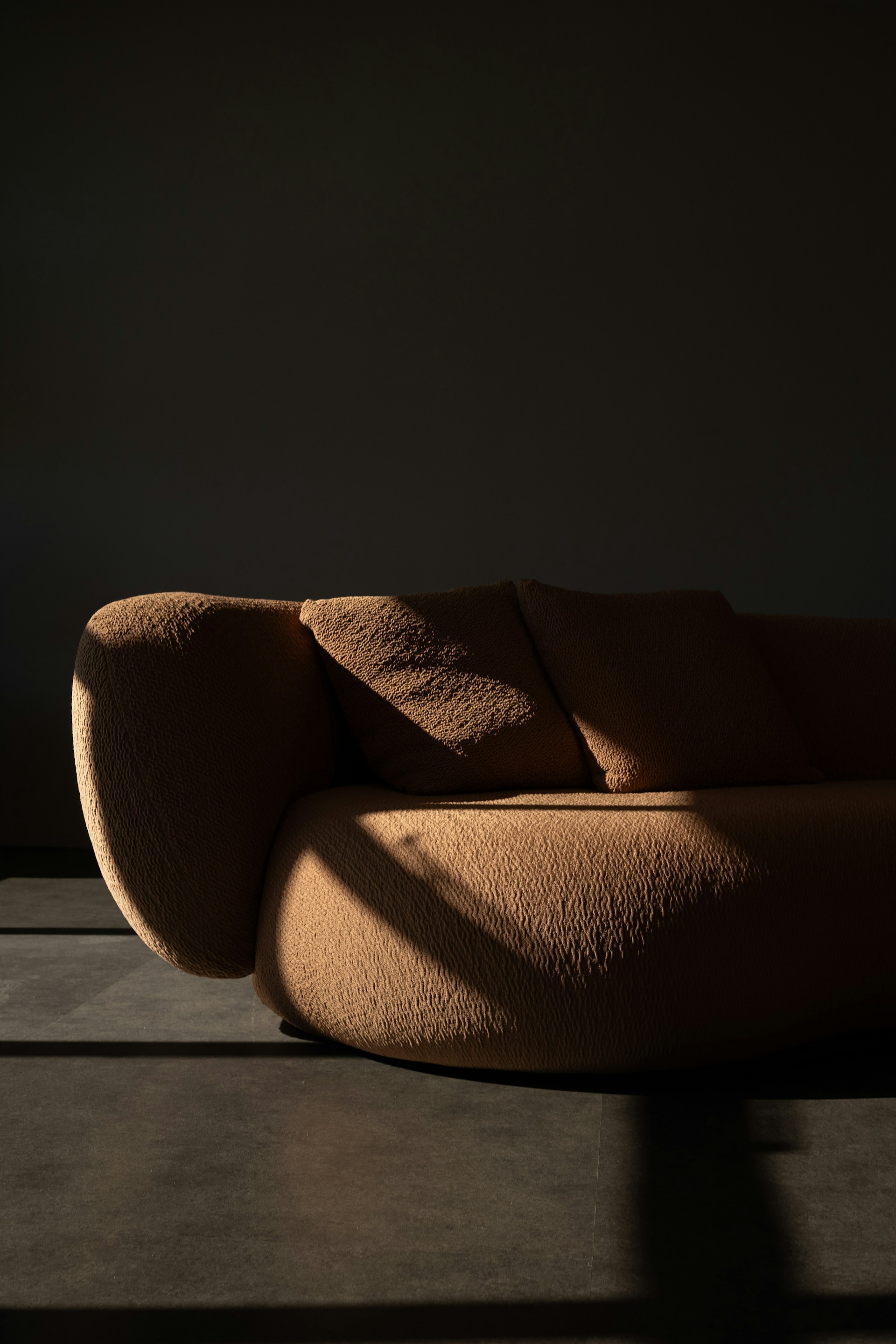 A textured brown sofa bathed in dramatic sunlight.