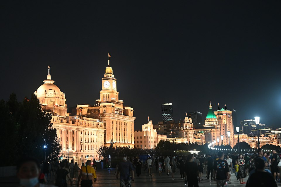 Ornate Bund buildings illuminated at night with crowds strolling the riverside promenade