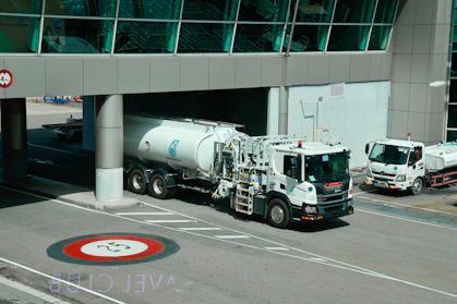 White tanker trucks drive under an airport structure.
