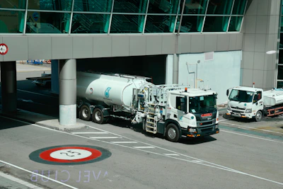 White tanker trucks drive under an airport structure.