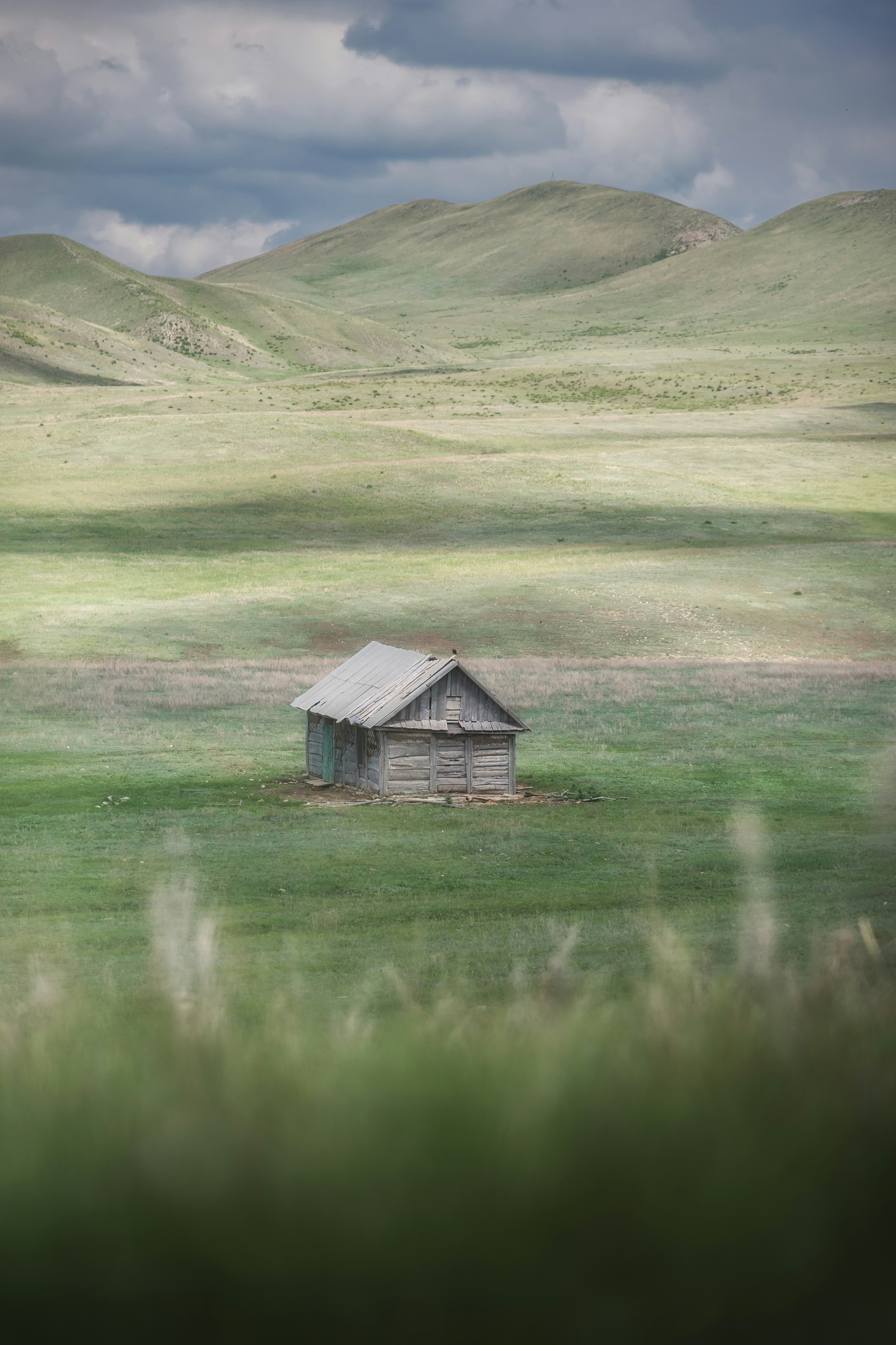Small wooden cabin in a vast, green, rolling landscape.