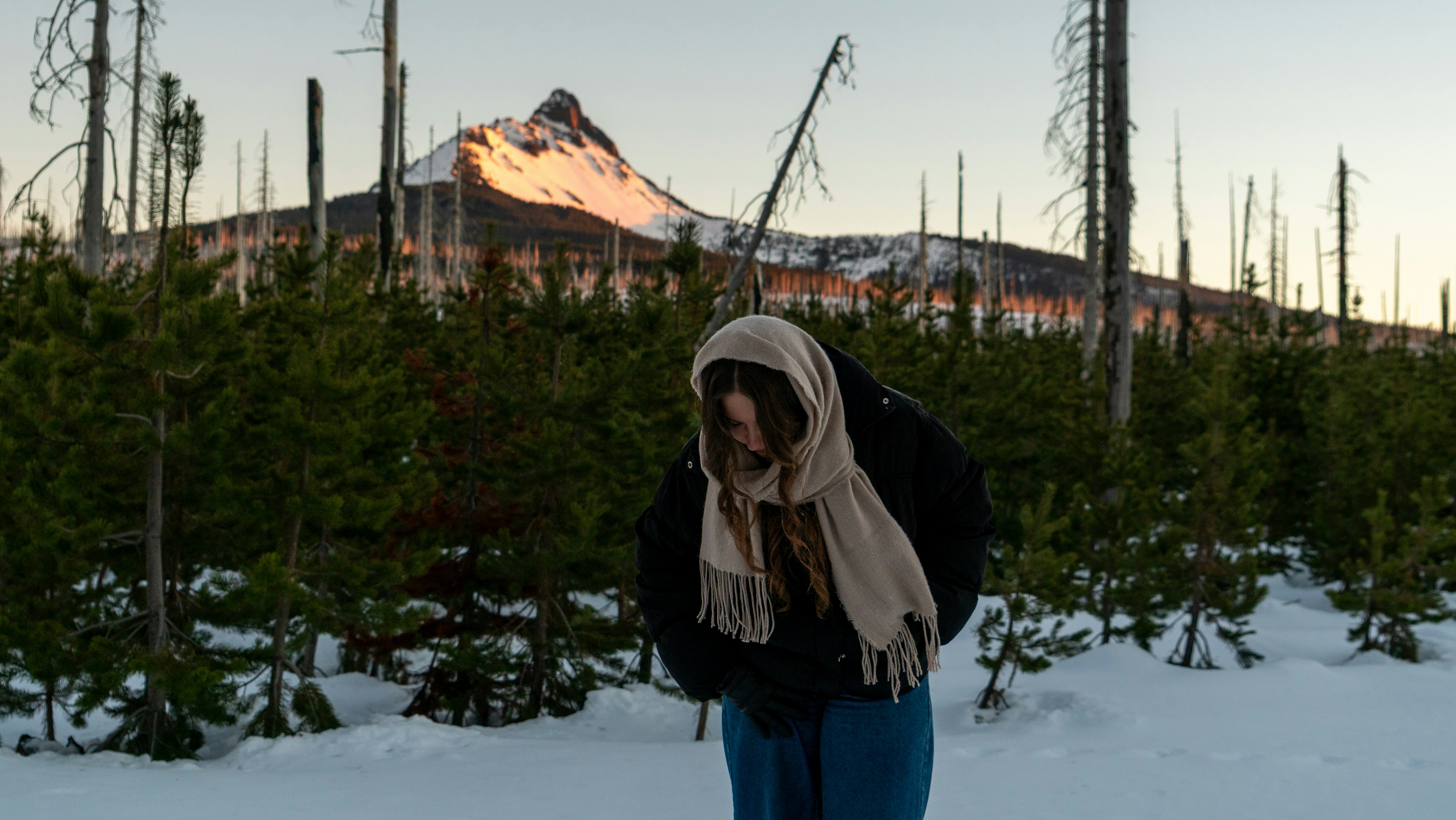 スカーフを巻いた女性が雪の森と山に立っている。