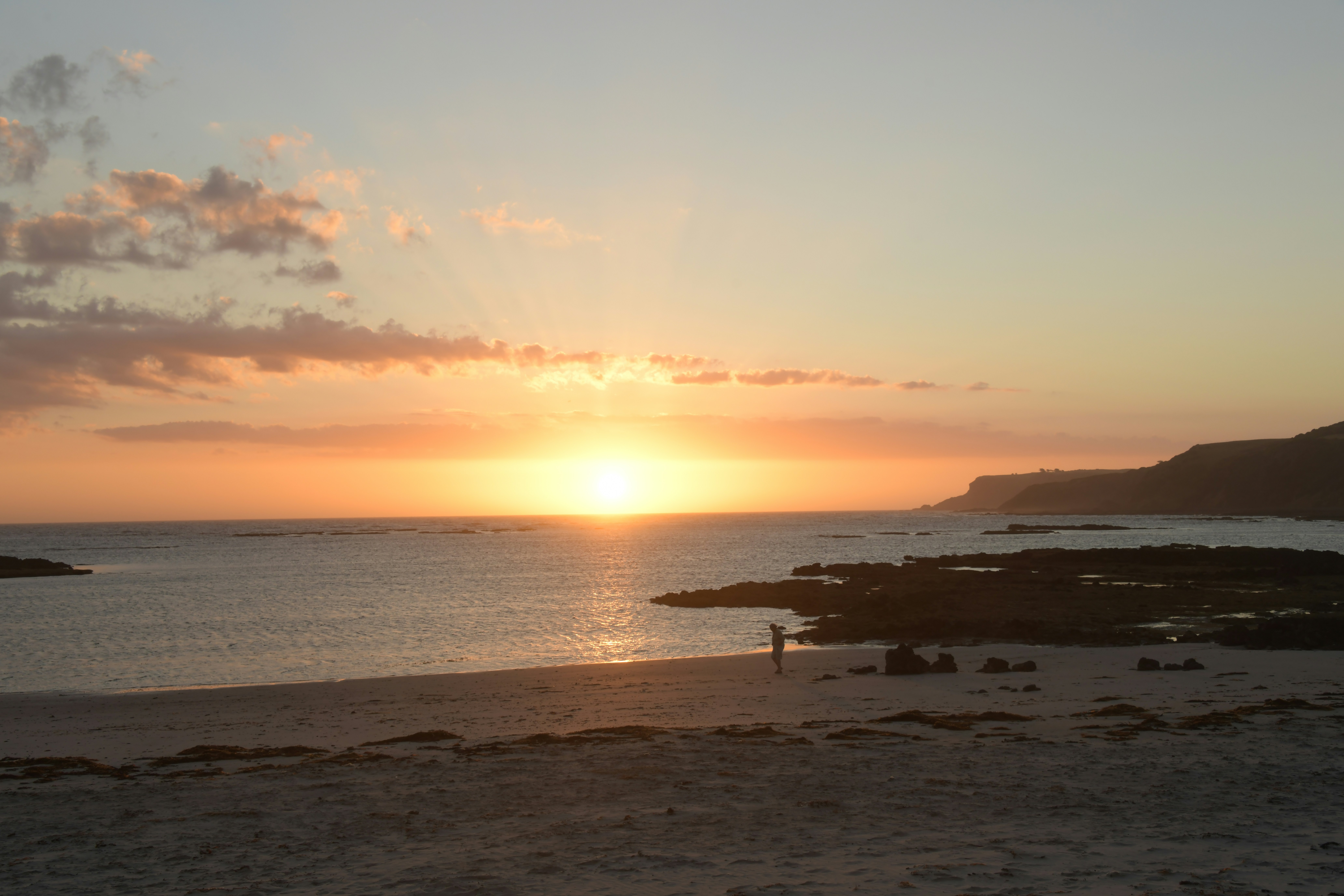 Coucher de soleil sur un océan calme avec une côte rocheuse.
