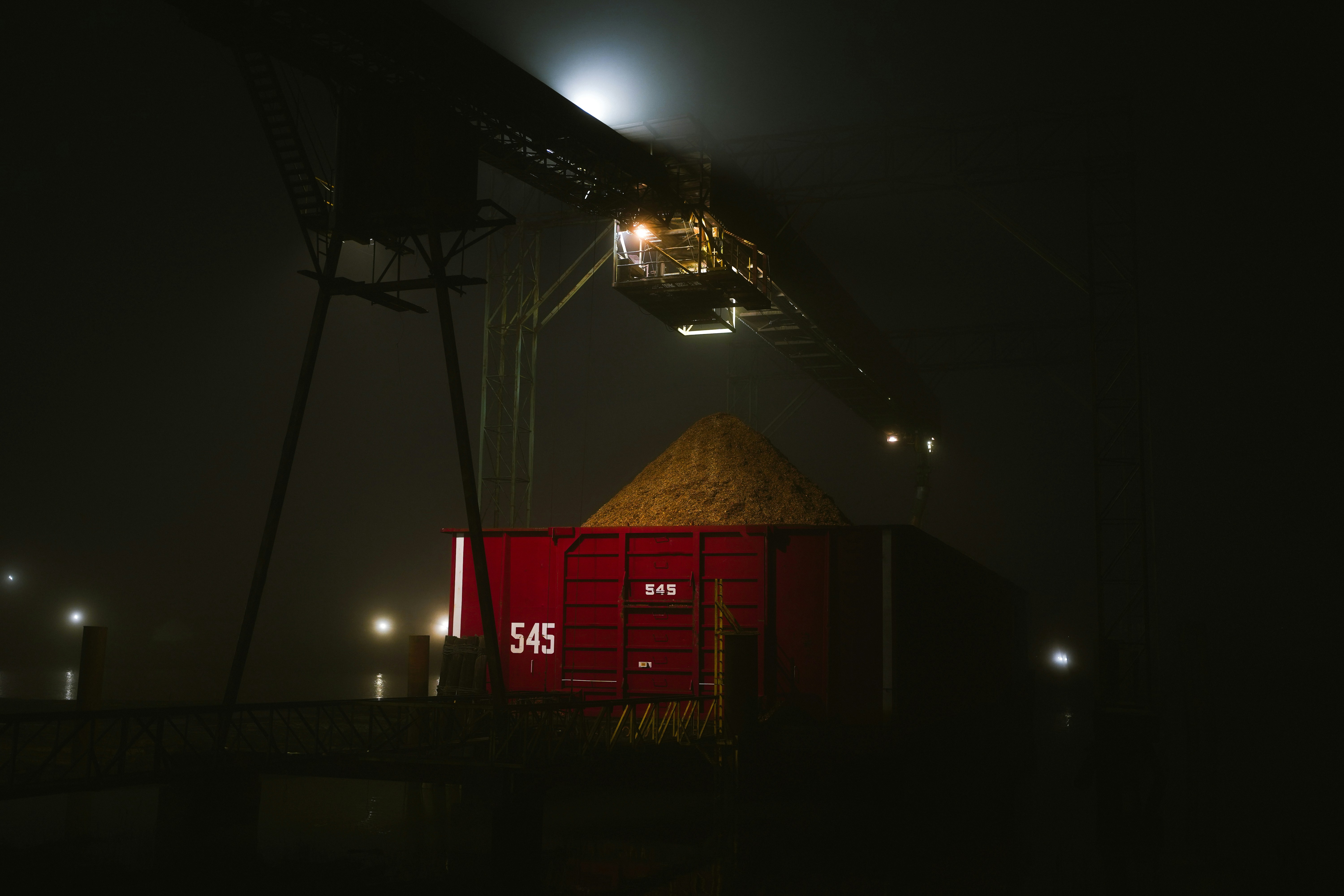 Grain being loaded into a red train car at night.