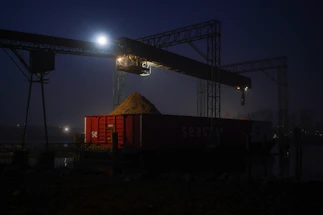 Industrial crane loading grain into a train car at night.